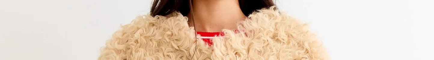 A person wearing a beige, curly faux fur coat over a red and white top, shown from the shoulders to just above the mouth.
