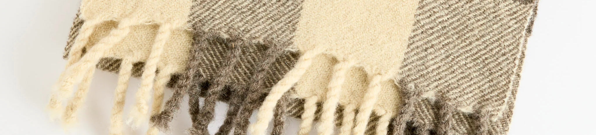 Close-up of a wool scarf with a beige and brown checkered pattern and fringed ends, displayed on a light background.
