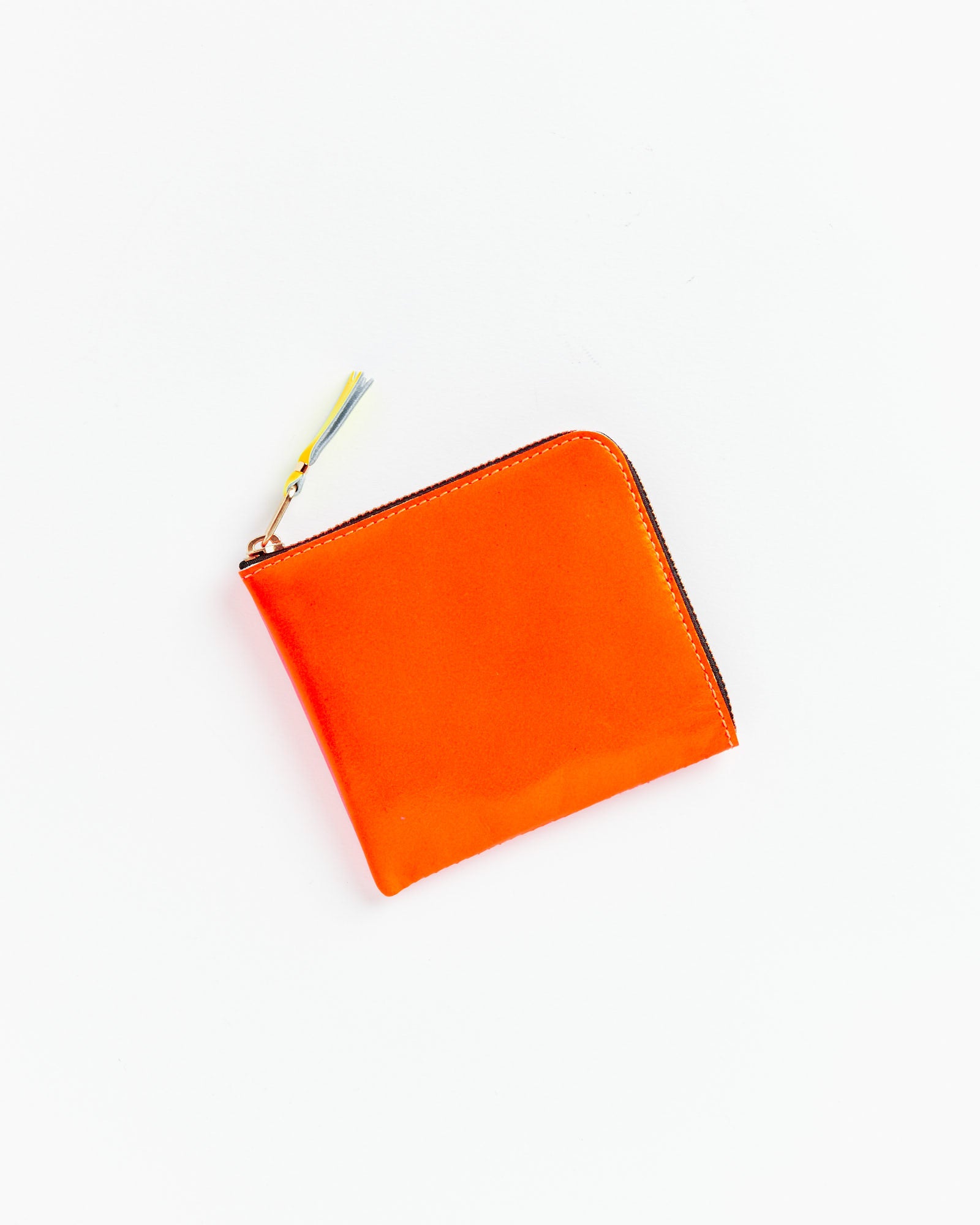 The Comme des Garcons Wallet Super Fluo Half Zip Wallet in Orange/Pink, made from premium goat leather in Spain, features a zip closure with tassel pull and is shown closed on a white background.