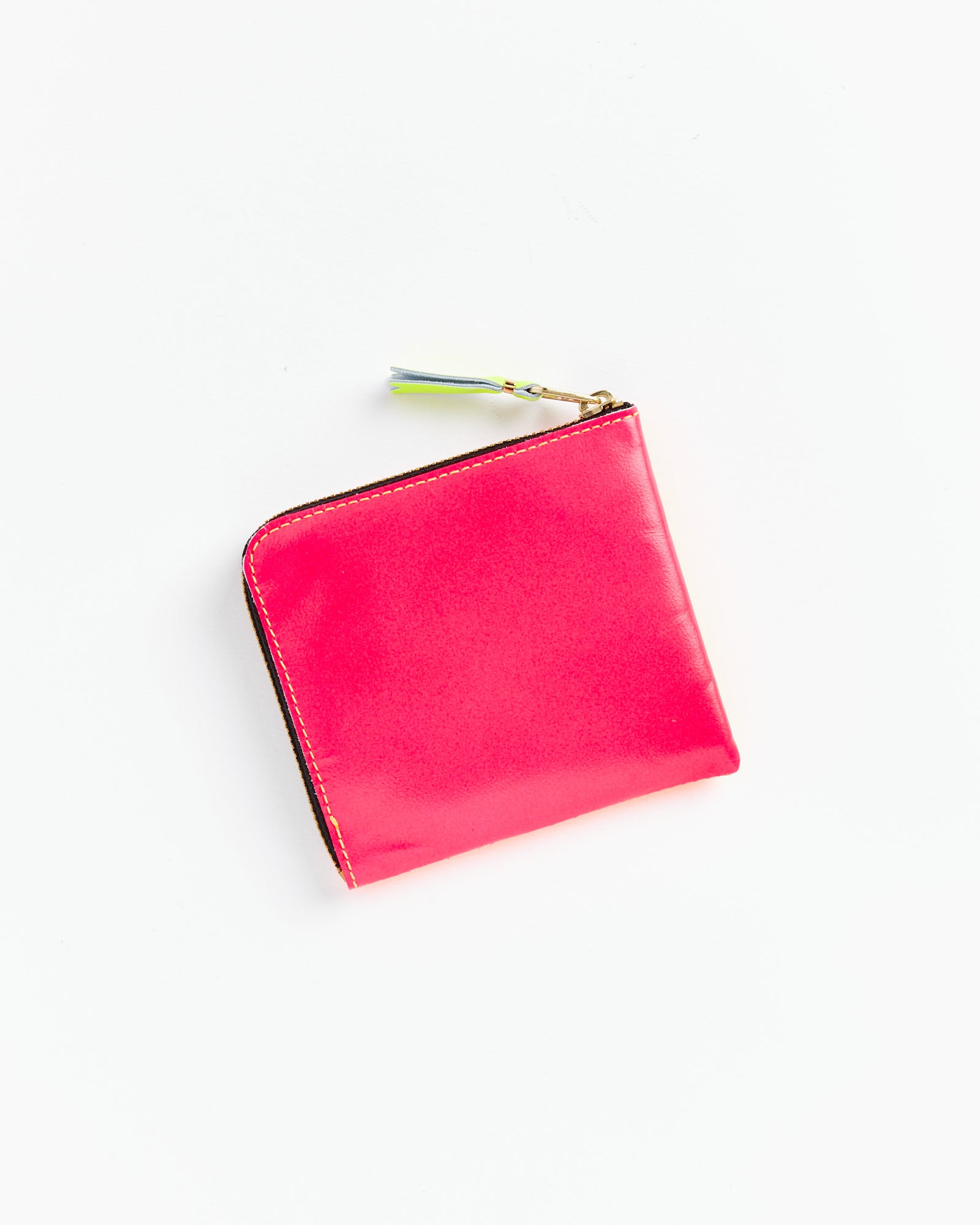 The Super Fluo Half Zip Wallet in Orange/Pink by Comme des Garcons Wallet is a square goat leather wallet made in Spain, featuring a small multicolored tassel on the zipper, shown on a white background.