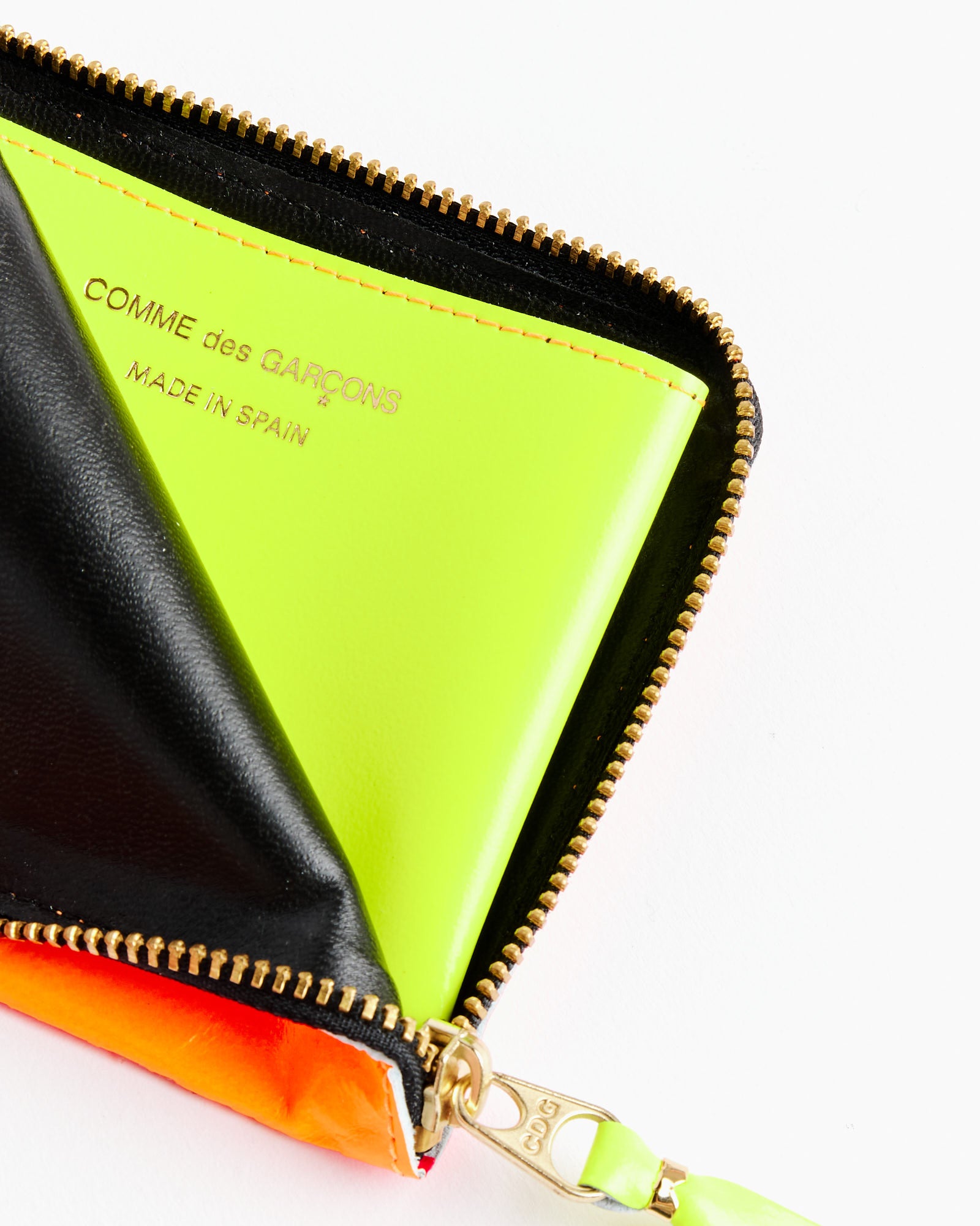 A close-up of a zippered pouch reveals the Comme des Garcons Wallet Super Fluo Half Zip Wallet in Orange/Pink. This goat leather wallet features gold text and a gold zipper with a leather pull.