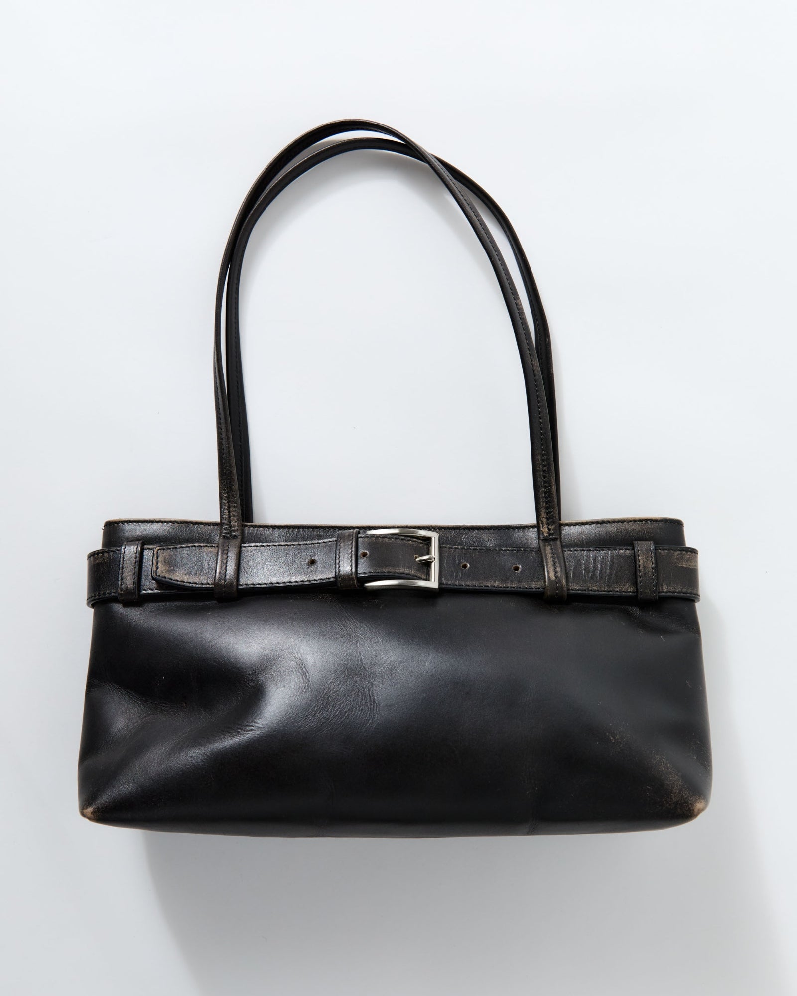 The ST. AGNI Brushed Belt Detail Baguette Bag is crafted from black bovine leather, features two long straps, a decorative top belt with a silver buckle, cotton lining, and is shown on a plain light background.