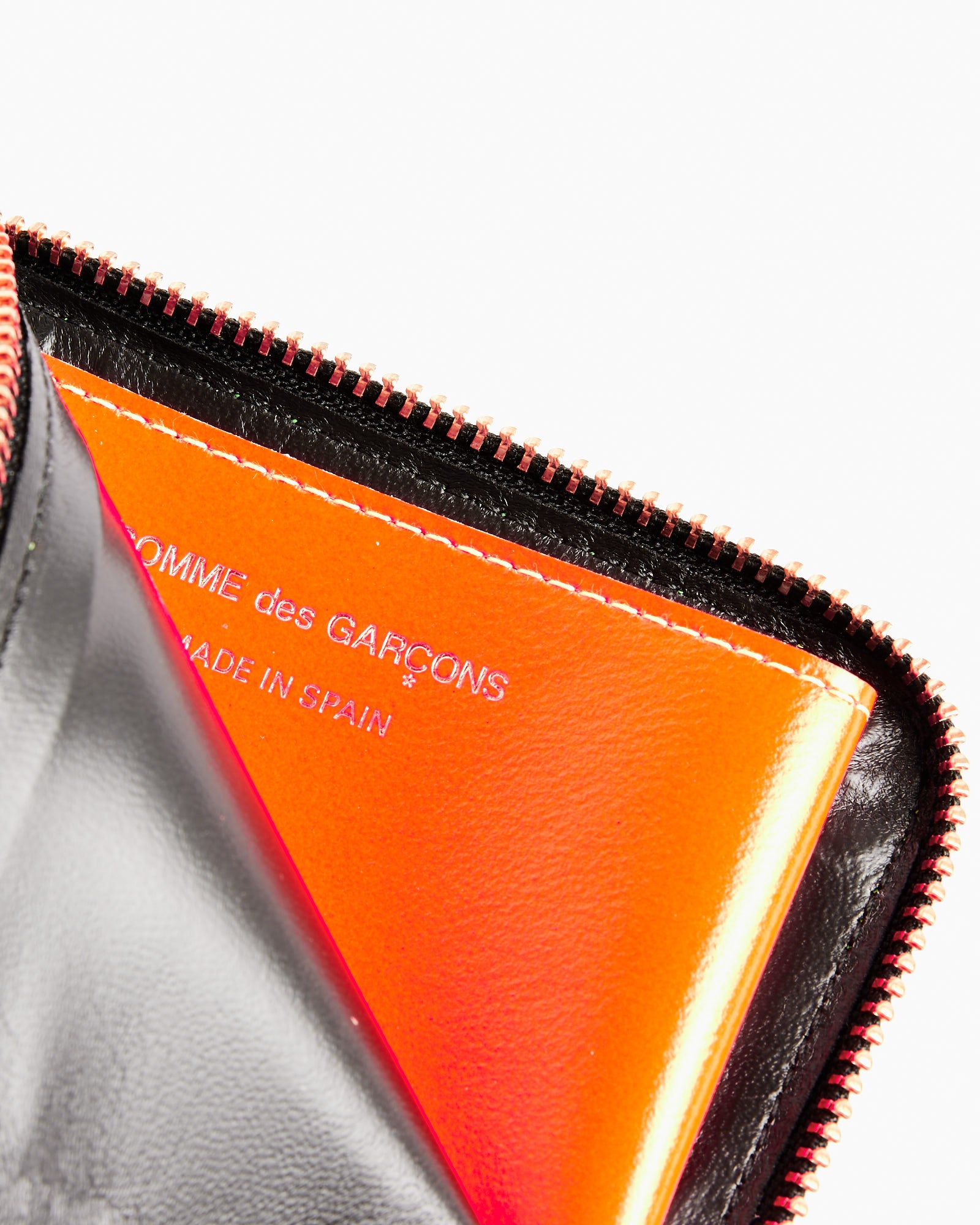 A close-up of the Super Fluo Half Zip Wallet in Blue/Green by Comme des Garcons Wallet, partially open to reveal an orange interior, stamped with white branding. This stylish goat leather wallet blends bold colors and premium craftsmanship.