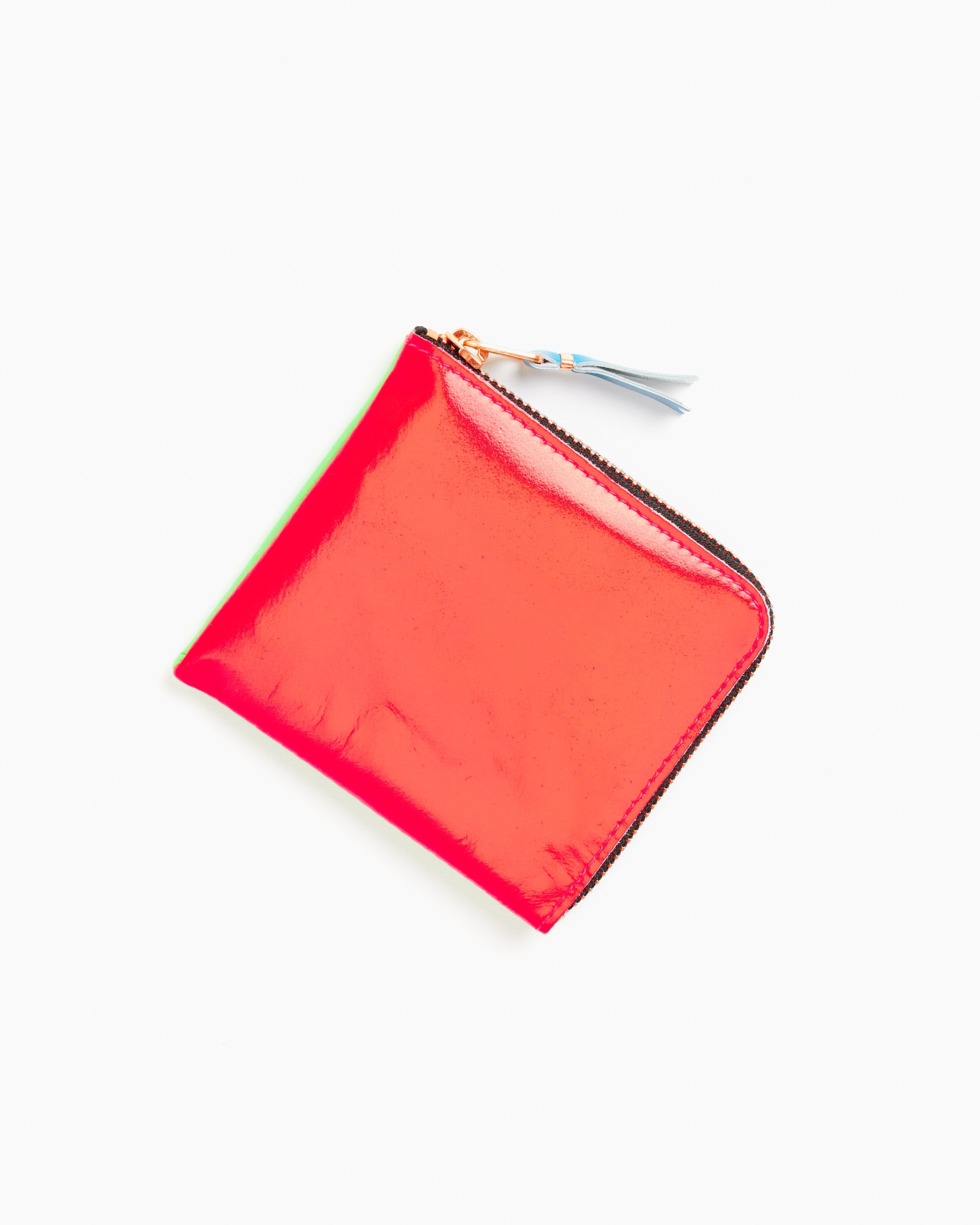 A Super Fluo Half Zip Wallet in Green/Orange by Comme des Garcons Wallet, made from premium goat leather with a tassel on the zipper, is displayed against a white background.