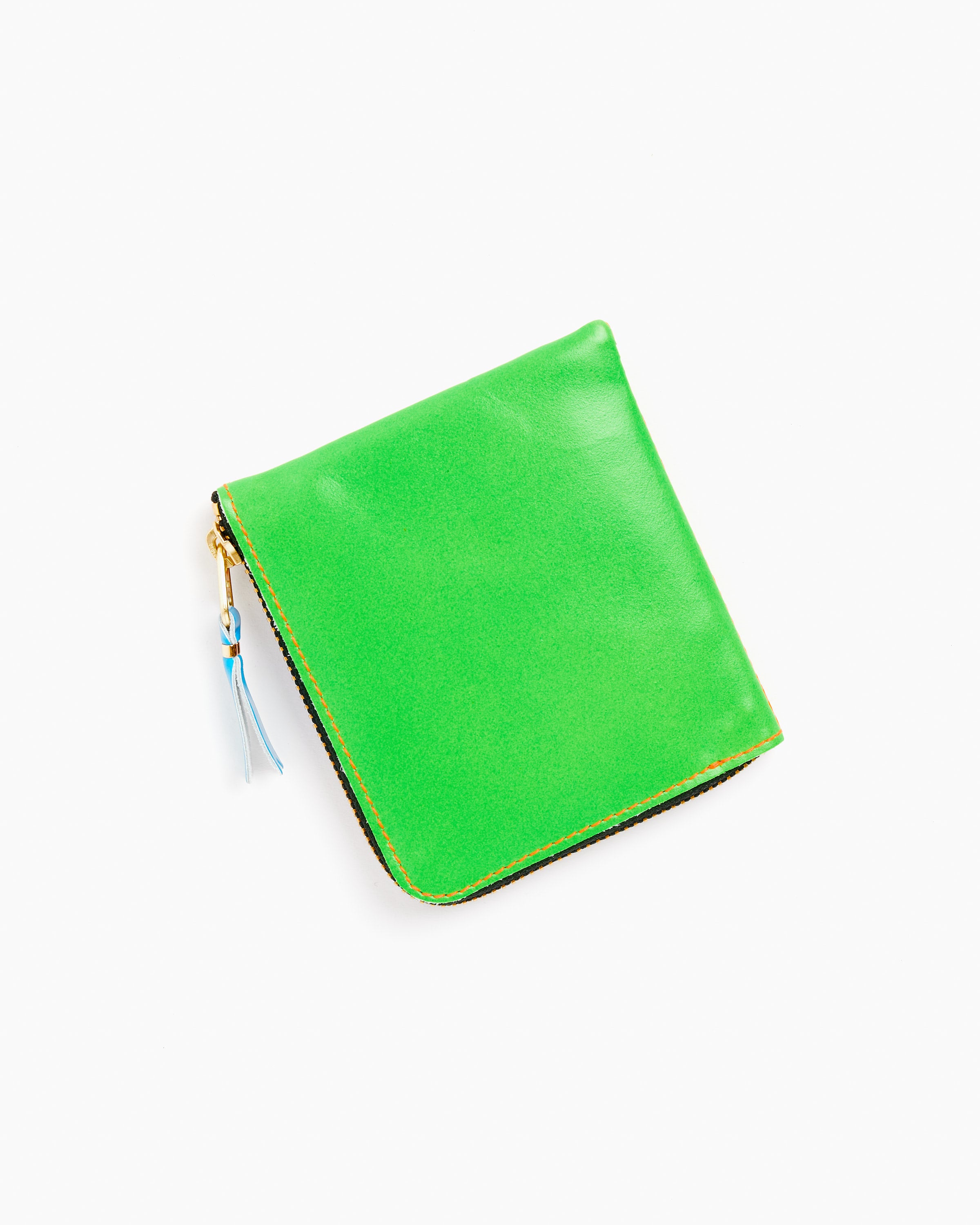 The Comme des Garcons Wallet Super Fluo Half Zip Wallet in Green/Orange, made from premium goat leather in Spain, features a zip closure with a blue tassel and is shown on a white background.