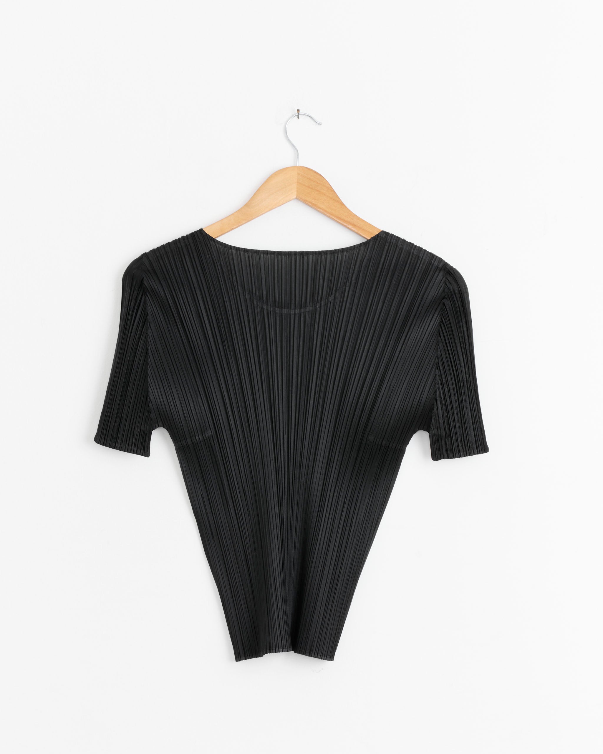 The Basics Top in Black by Pleats Please Issey Miyake, featuring short sleeves and signature pleats, hangs on a wooden hanger against a plain white background.