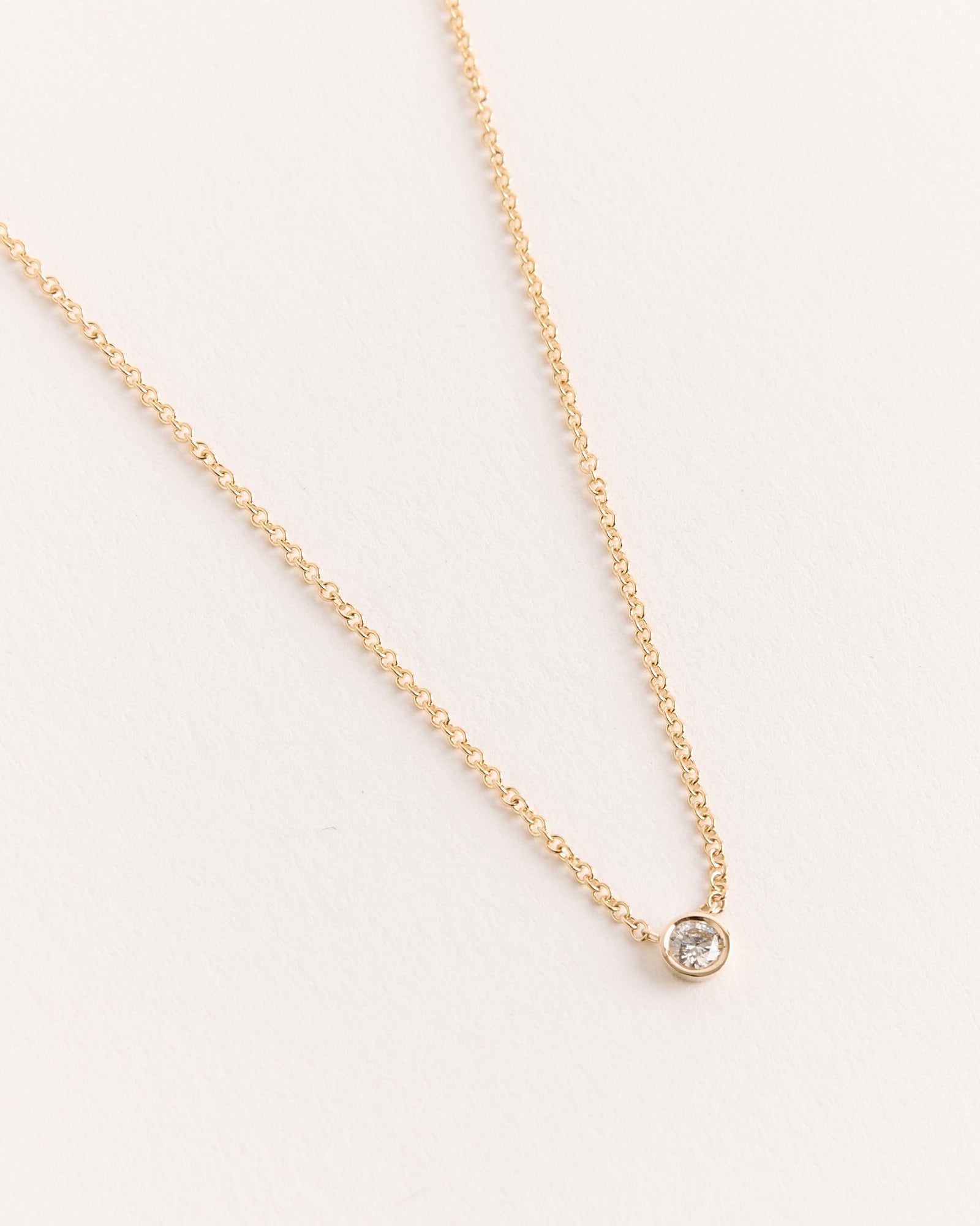 The Hortense Solitaire Necklace features a small, round bezel-set diamond pendant on a delicate 14k yellow gold chain. Handmade in Los Angeles, it's beautifully displayed against a light background.