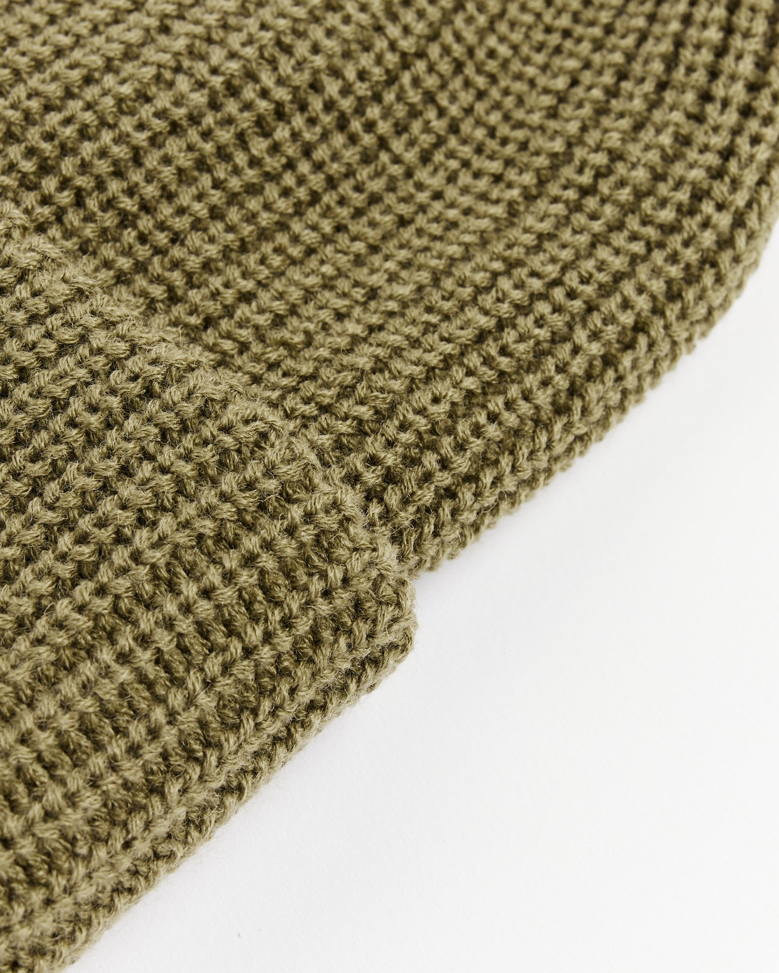 A close-up of the textured, light olive knit fabric from the Rototo 5075 Chunky Beanie, shown folded on a plain white background.