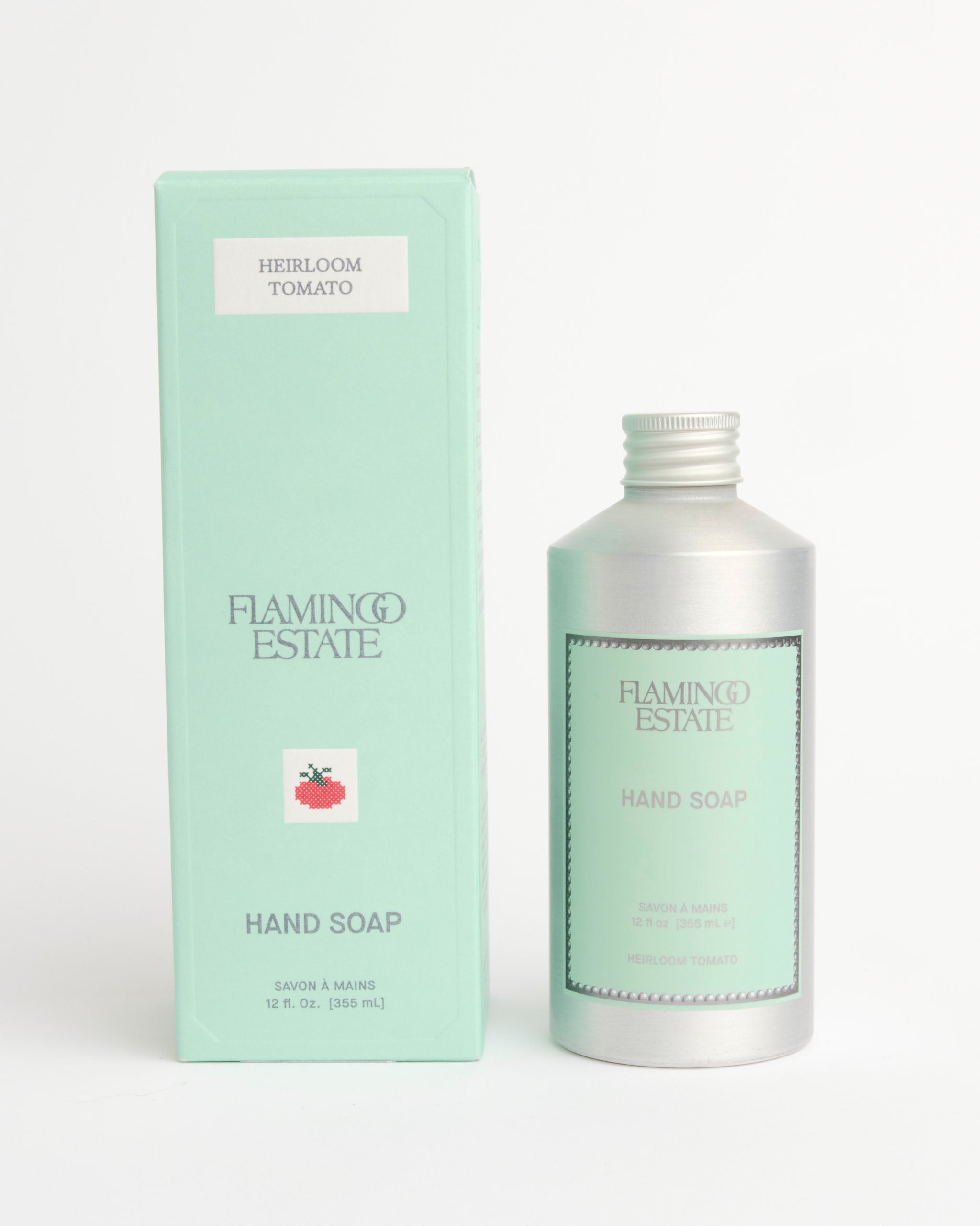 A light green box and a silver bottle, both labeled Flamingo Estate Heirloom Tomato Hand Soap, feature a tomato graphic and highlight nourishing olive oil in the formula.