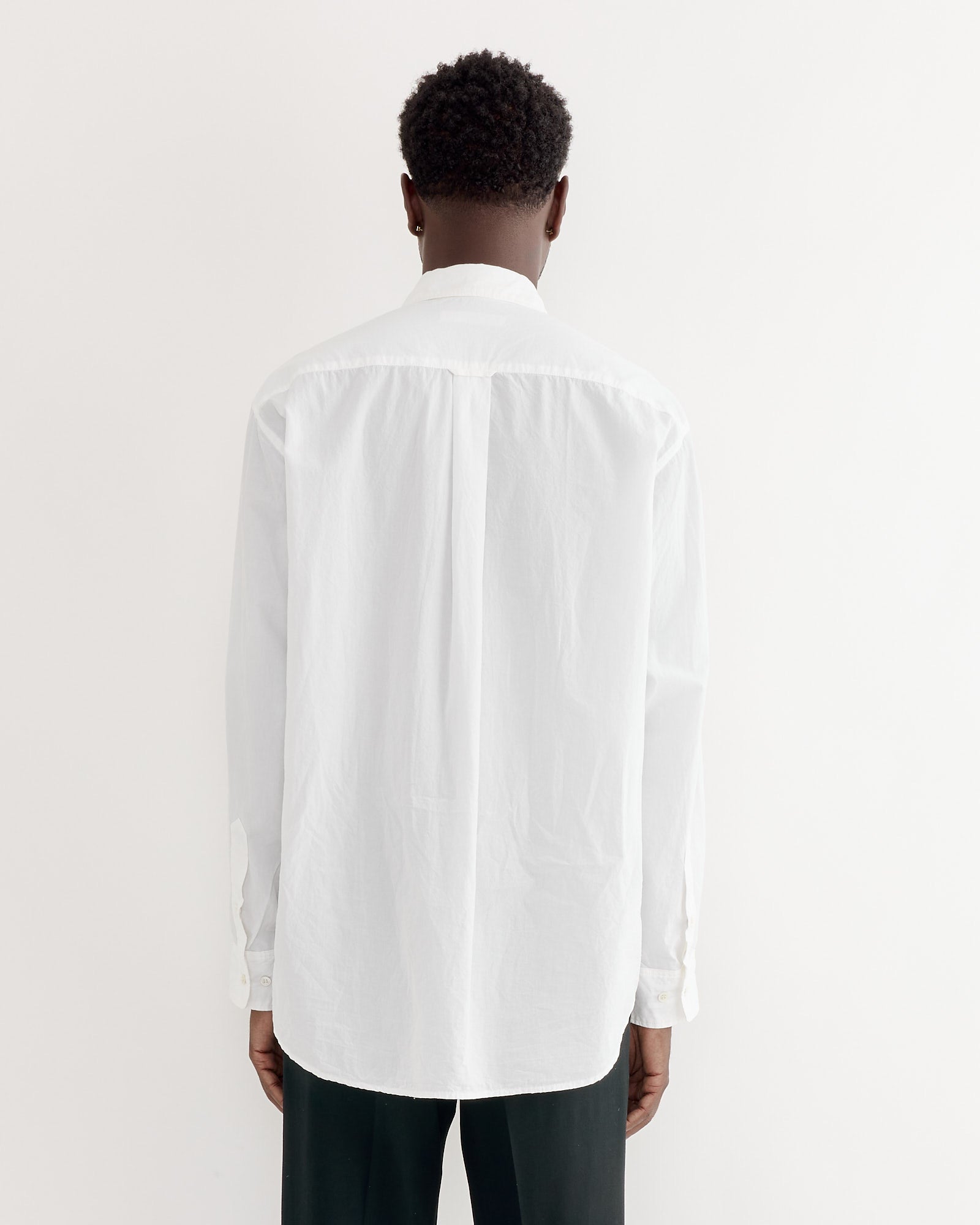 A person faces away from the camera, wearing the SMOCK Gio Shirt in Crushed Cotton White with a boxy fit and dark pants, set against a plain white background.