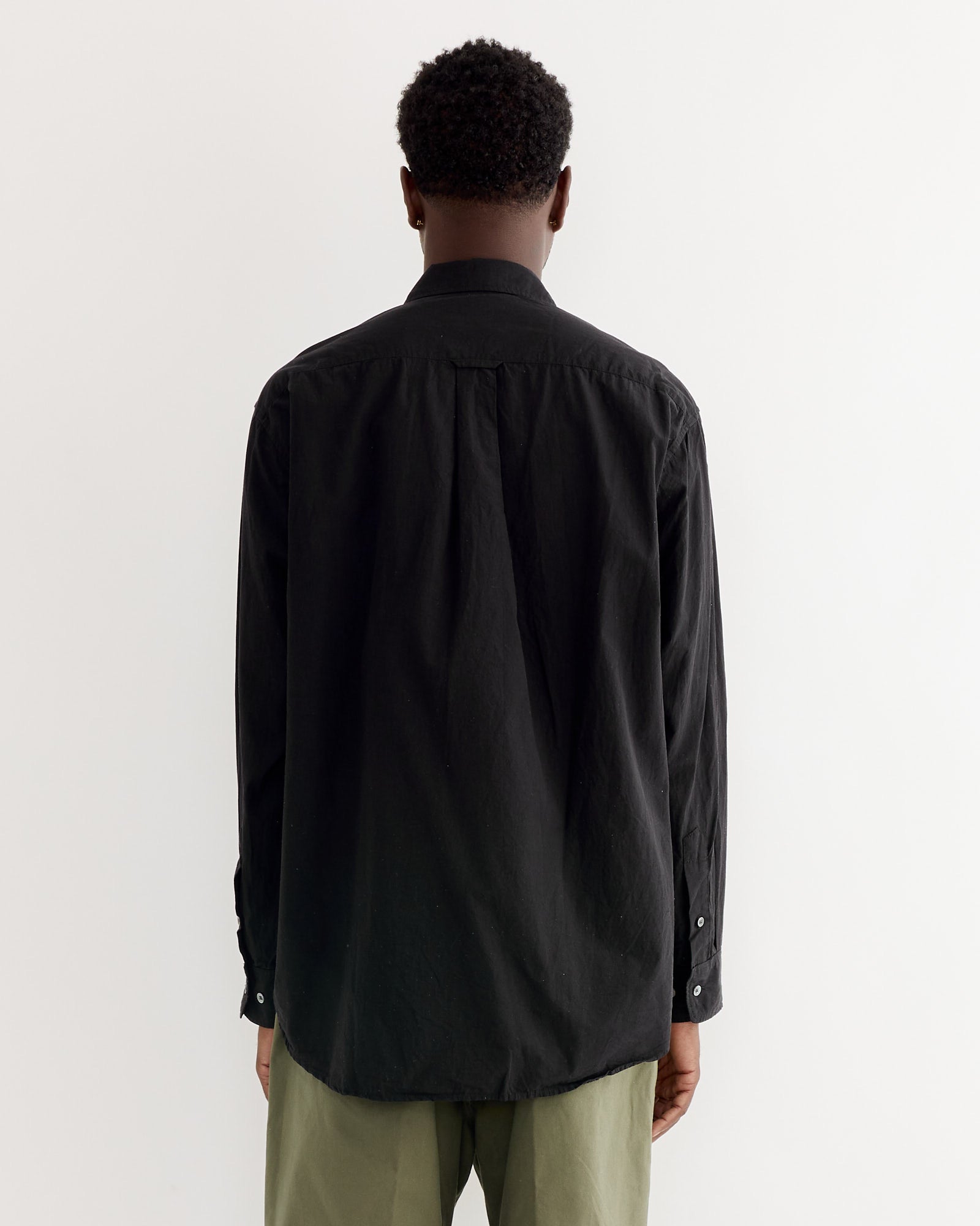A person with short curly hair, facing away from the camera, wears the SMOCK Gio Shirt in Crushed Cotton Black and light olive green pants against a plain white background.