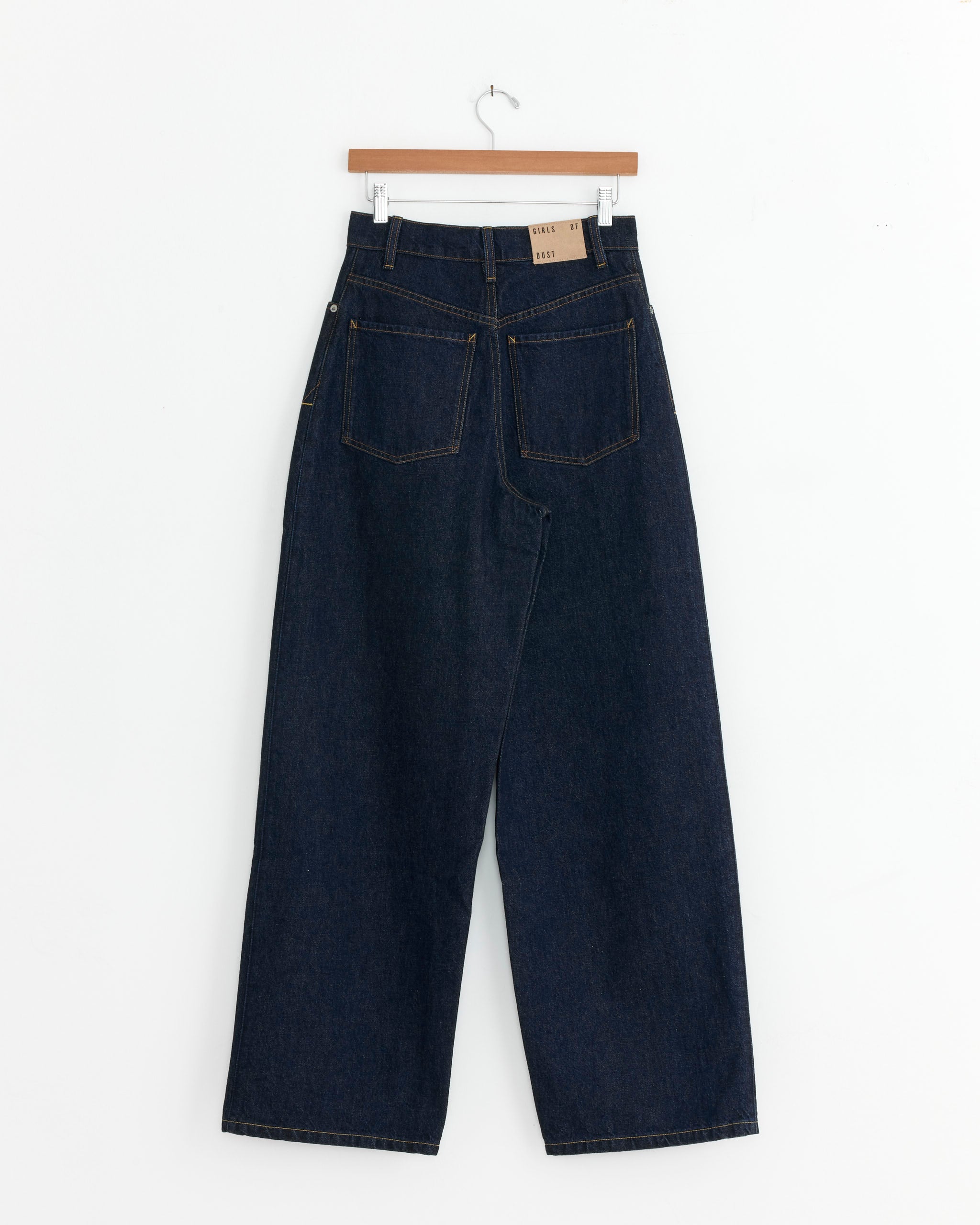 The Janet Jean in Blue by Girls of Dust, featuring wide legs and large back pockets, hangs on a wooden hanger against a white background.