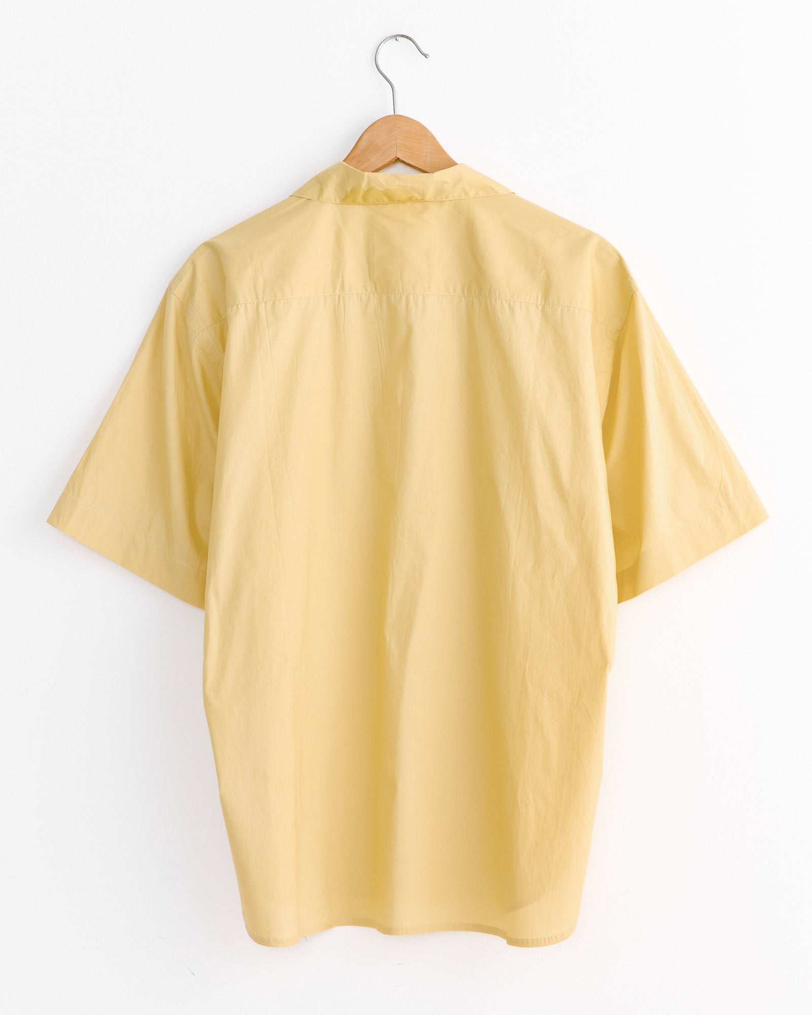 The Kardo Ronen Embroidery Shirt in Flower, a short-sleeved light yellow top with traditional floral Chikankari motifs, is displayed on a wooden hanger against a plain white background, viewed from the back.