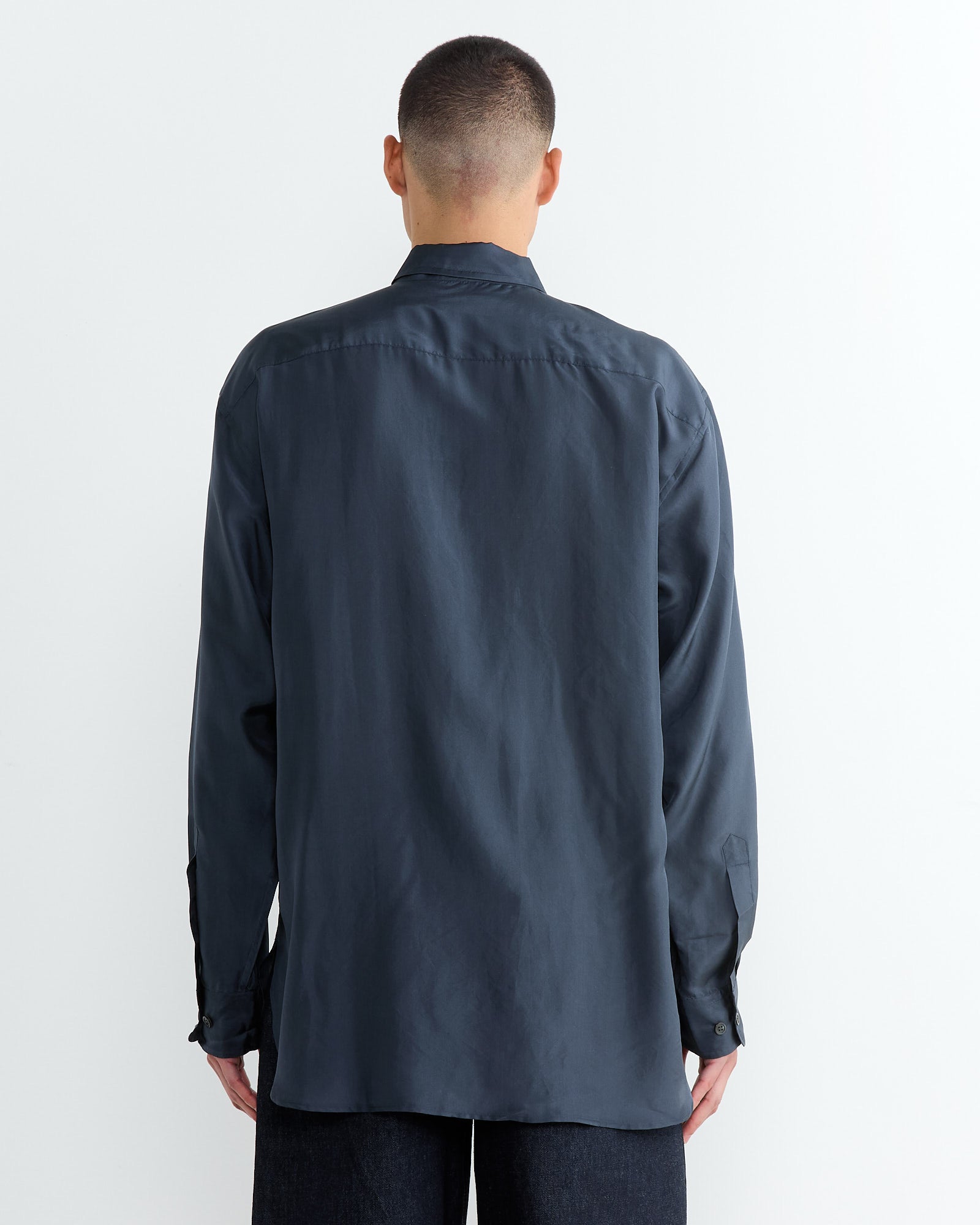A person wearing a Dries Van Noten long-sleeve shirt in navy stands with their back to us. They have short hair and are positioned against a plain white background.