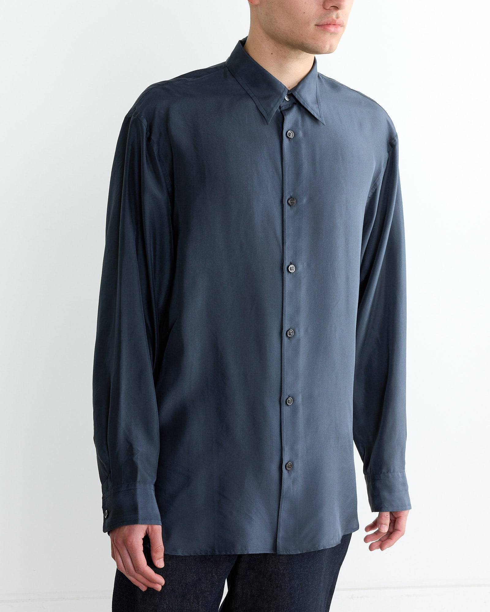 Against a plain white background, a person stands wearing Dries Van Notens Long-Sleeve Shirt in Navy, buttoned to the collar with a loose fit, paired with dark pants; their face is not visible.