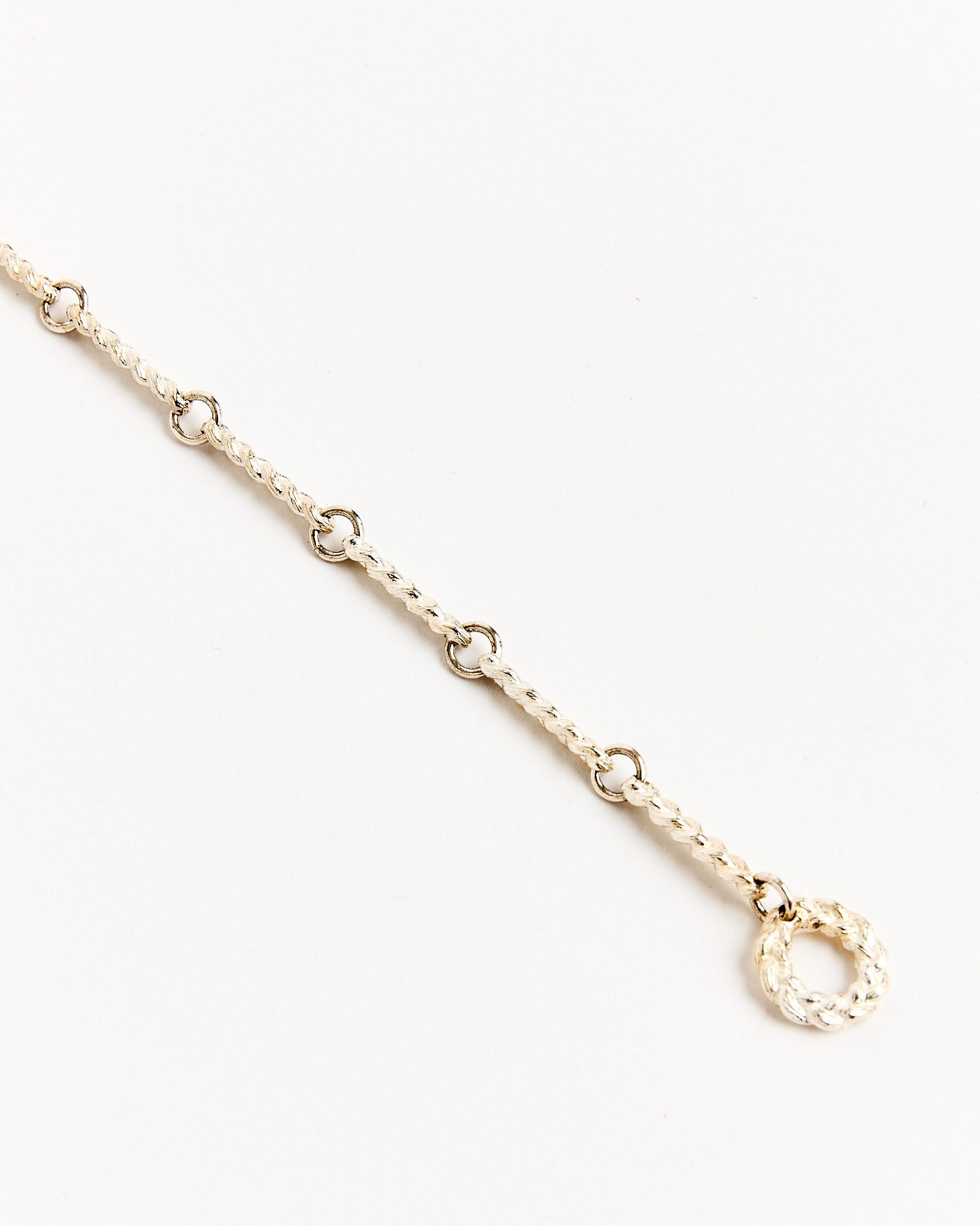 The Braided Link Bracelet in Silver by Bleue Burnham features delicate, evenly spaced links on a silver chain with a textured circular clasp, displayed against a plain white background.