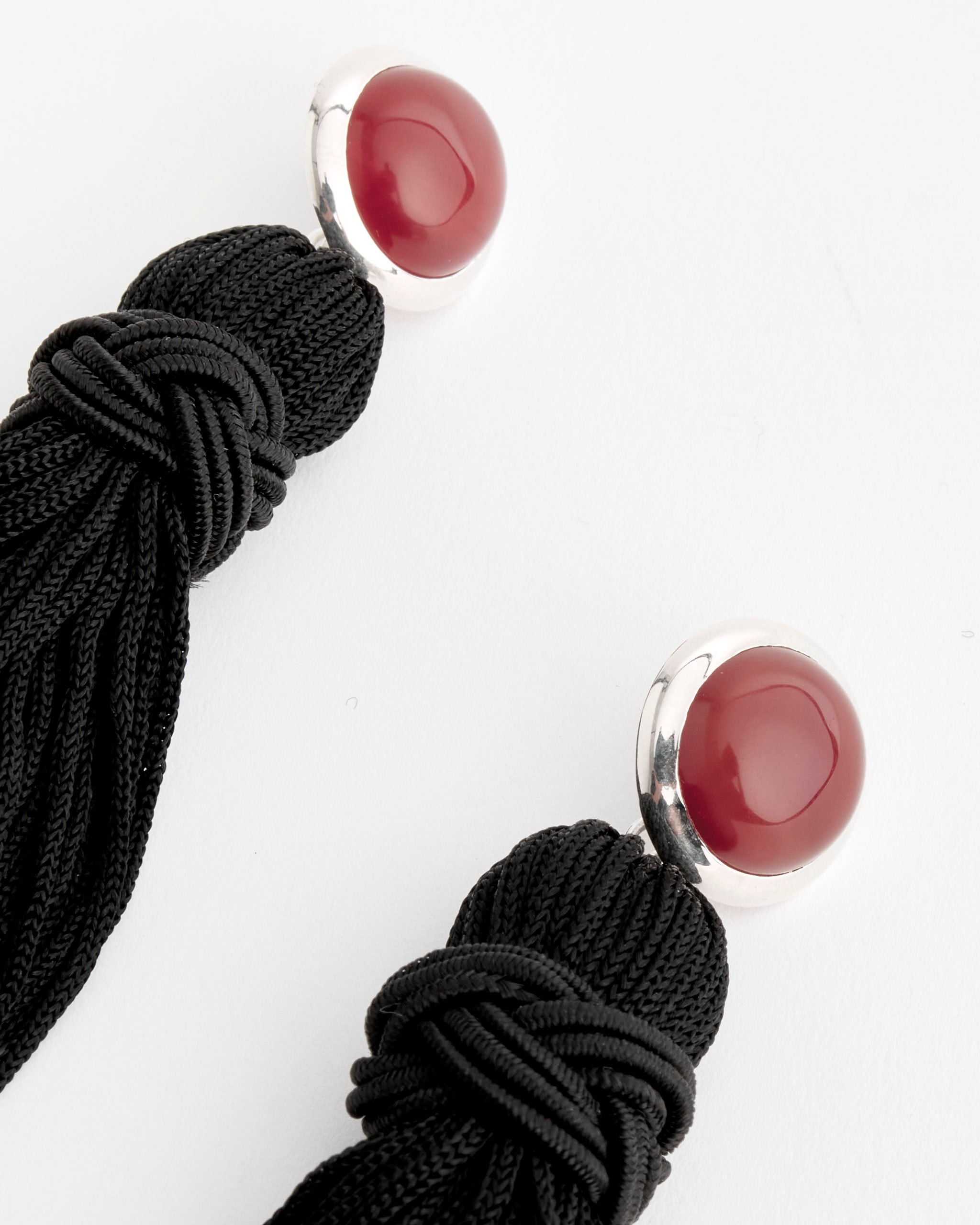 Close-up of Sophie Buhai Cleo Tassel Carnelian Earrings, showing glossy red cabochons in sterling silver with black cord tassels, against a plain white background.