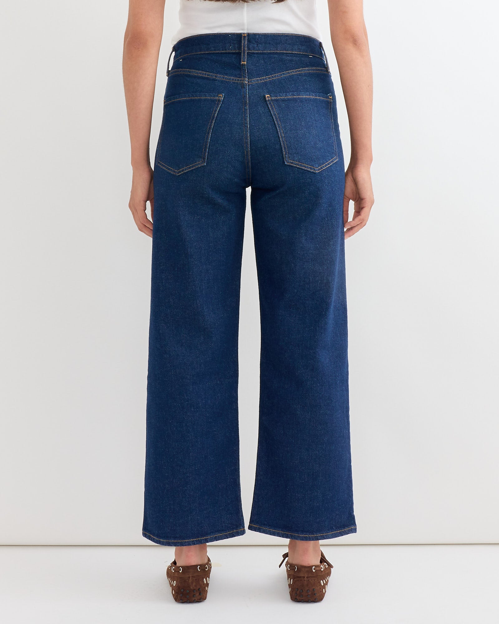 A person faces away, wearing AGOLDE's Ren Jean in Reissue—sustainable high-waisted, wide-leg blue jeans with back pockets—and brown platform sandals, set against a plain white background.