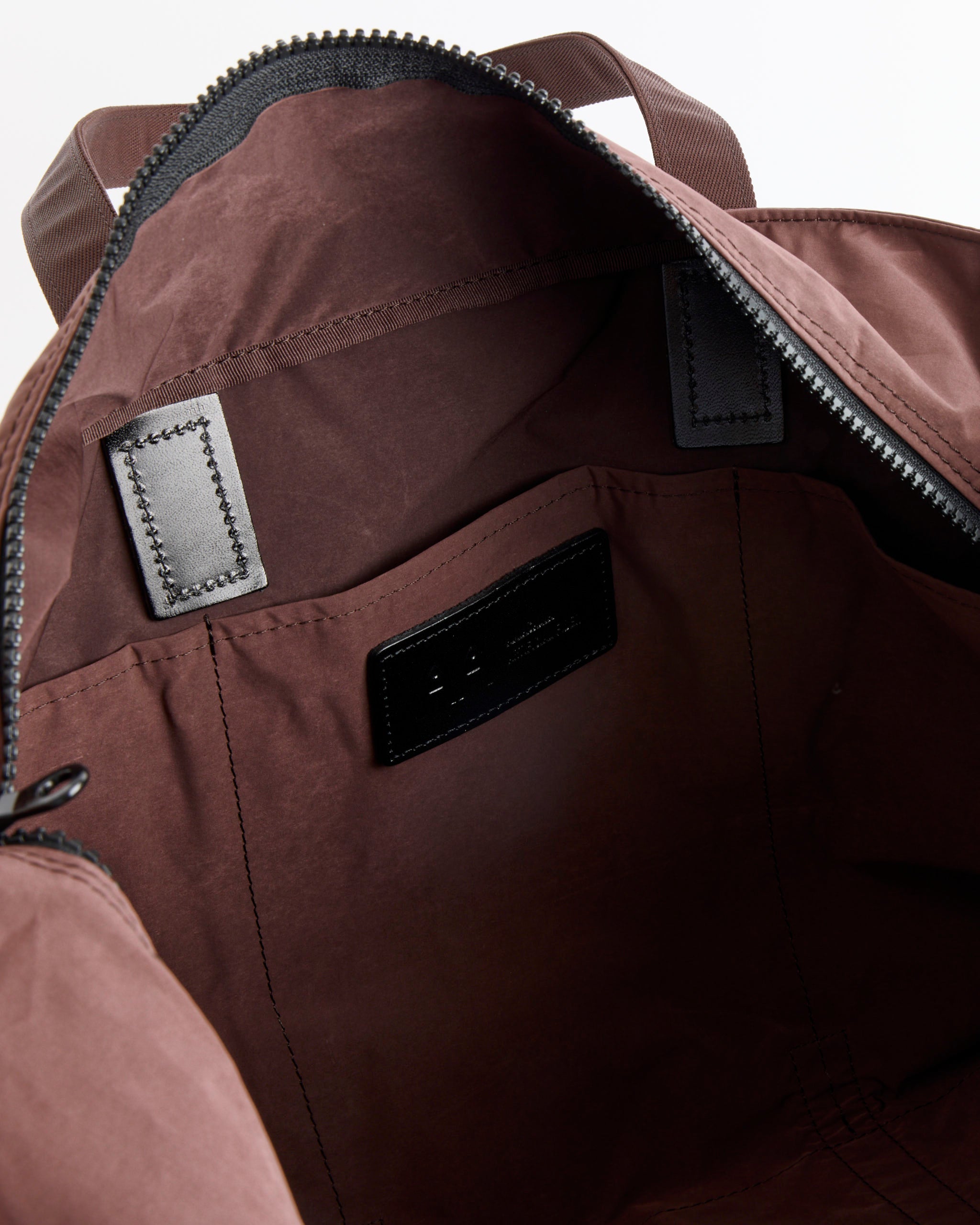Open view of the Amiacalva Gabardine Tote in Bordeaux Brown, showcasing its spacious interior, a small inner pocket, black stitching, and a visible black label inside near the zipper.