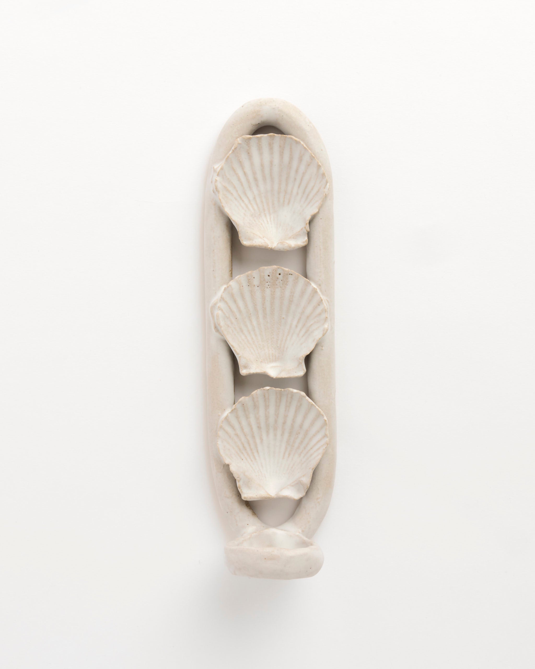 The Shell Sconce by Beau Rush Ceramics features three scallop shell shapes arranged vertically inside an elongated oval frame, all in a smooth off-white finish, set against a plain white background.