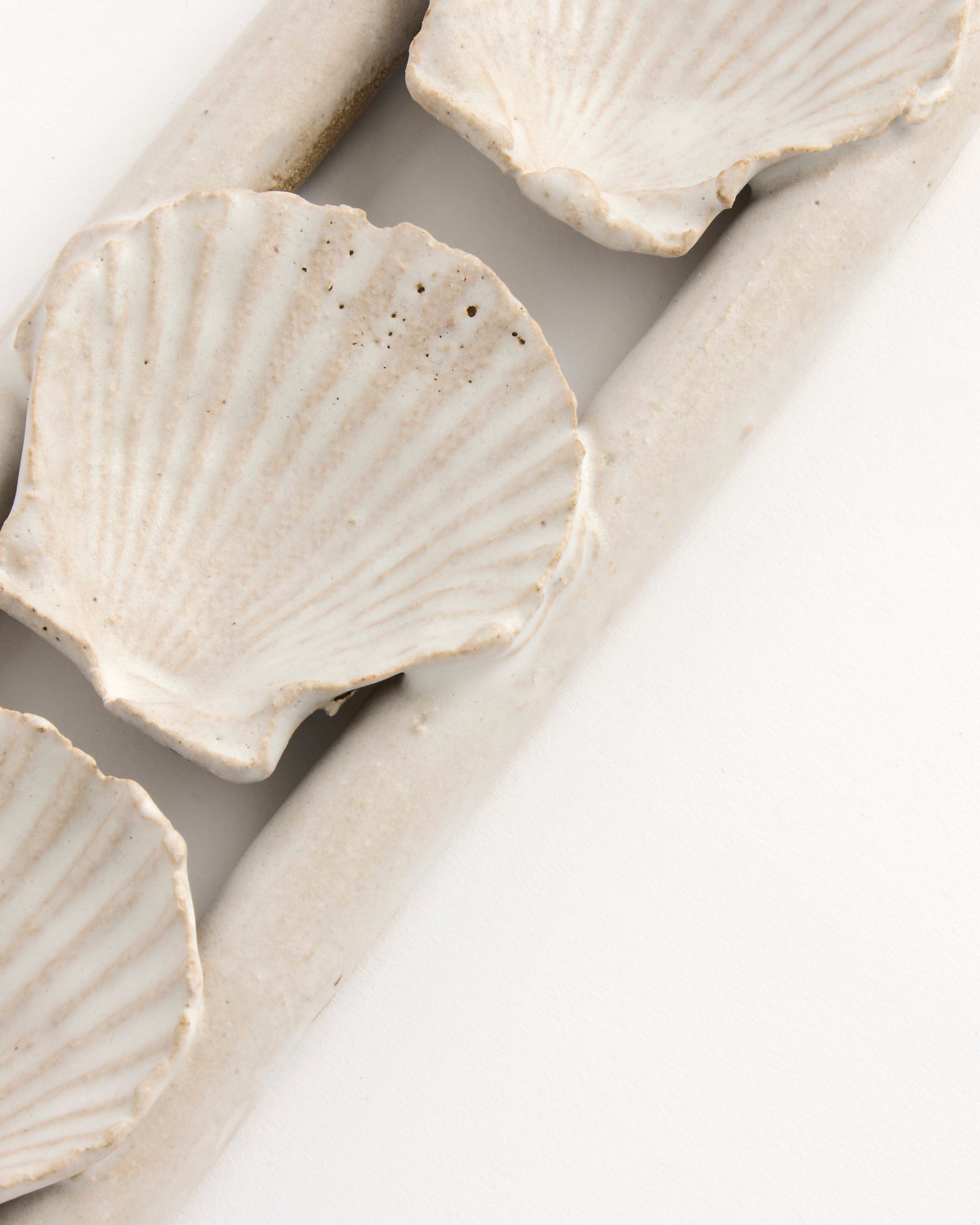 Close-up of the Shell Sconce by Beau Rush Ceramics, a ceramic dish shaped like scallop shells, resting on a rectangular off-white tray and viewed from above on a white background.