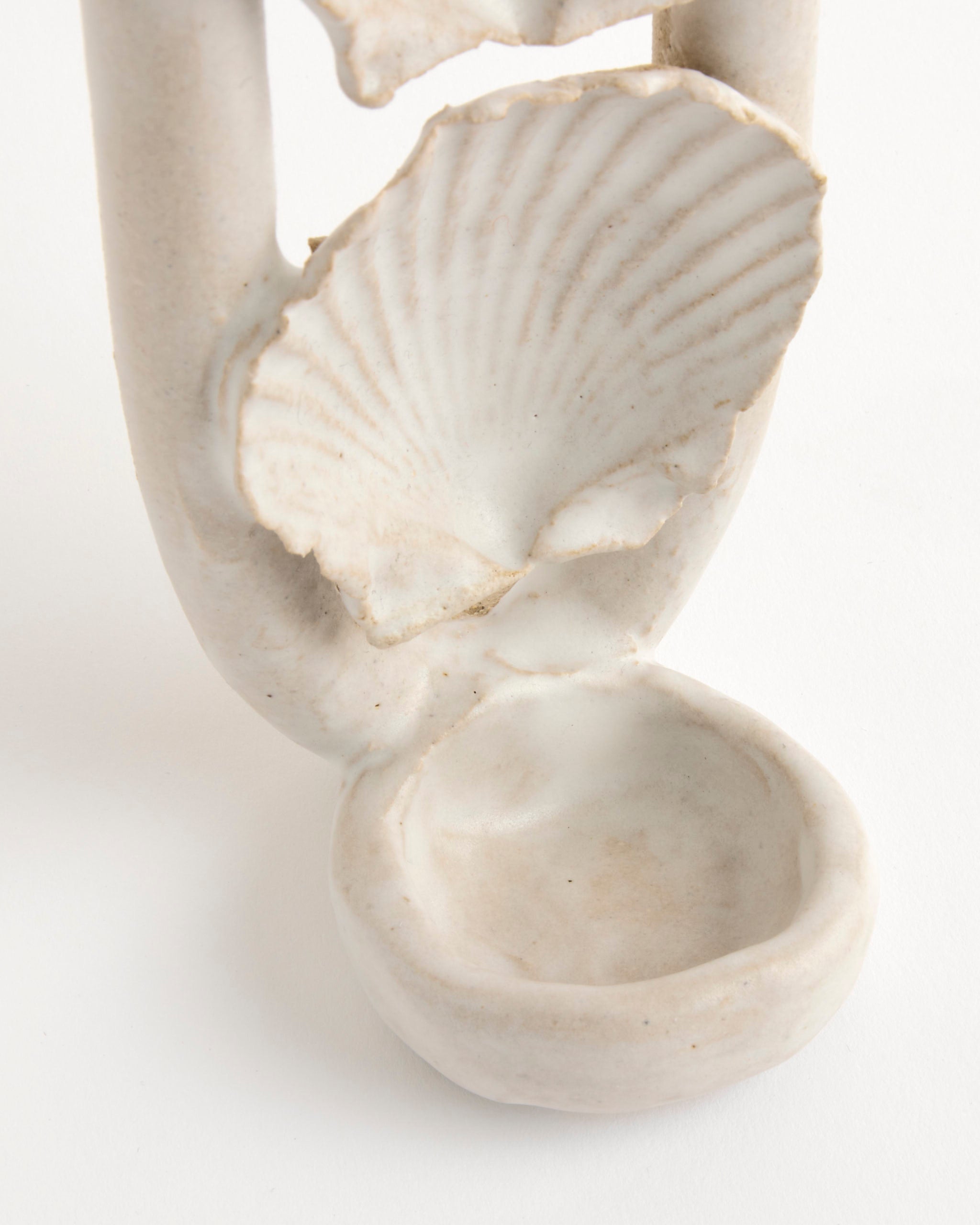 A close-up of the Shell Sconce by Beau Rush Ceramics shows a shallow bowl with a textured seashell shape above it, both glazed in off-white. The piece is set against a plain white background.