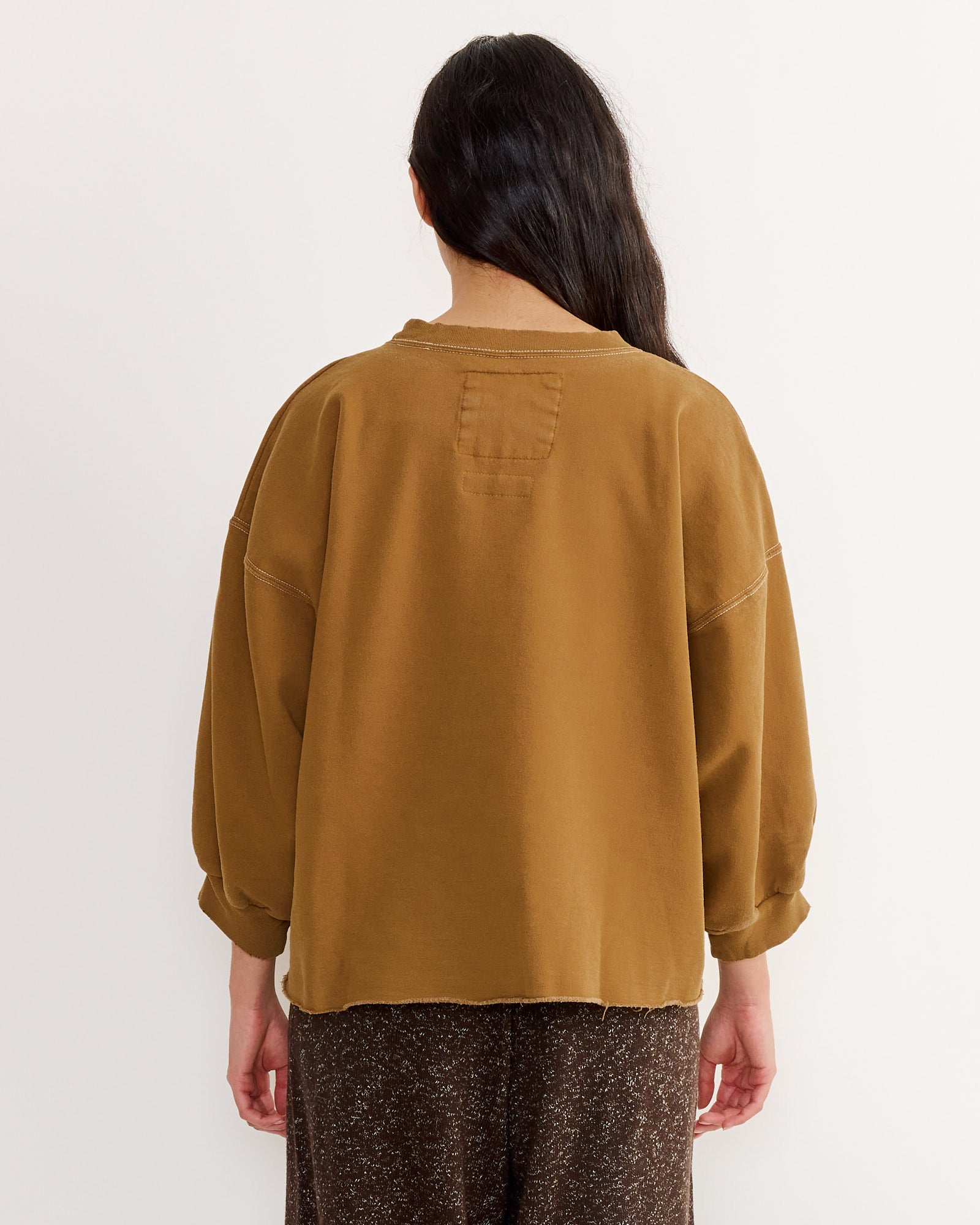 A person with long dark hair faces away, wearing the Rachel Comey Fond Sweatshirt in Bronze and dark speckled pants, size XS/S (25 waist, 27 inseam), against a plain white background.