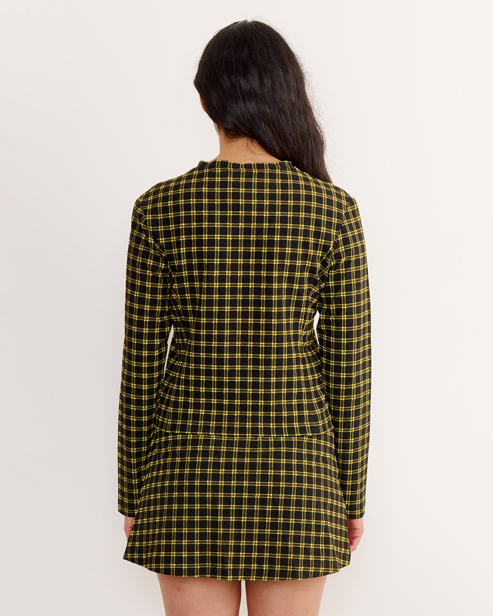 A woman with long dark hair faces away, wearing a size S Rachel Comey Satellite Top in black, set against a plain light background.