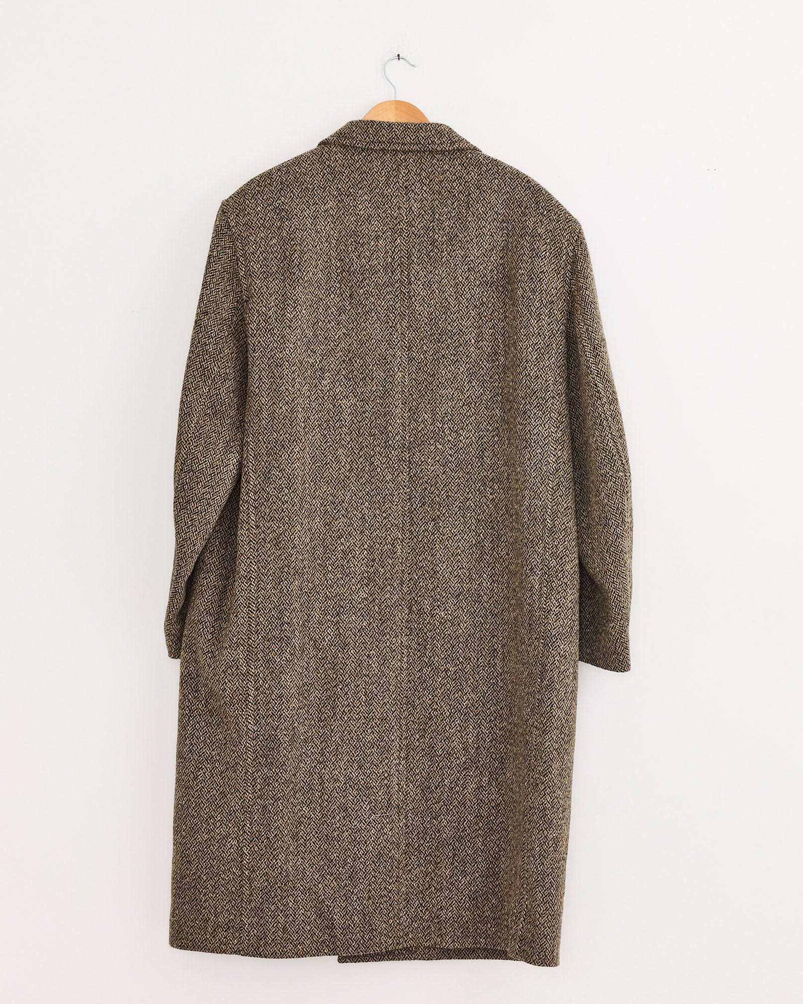 A Lemaire Chesterfield Coat in Black/Straw Melange, featuring a long, oversized silhouette, hangs from a wooden hanger against a plain white wall, shown from the back.