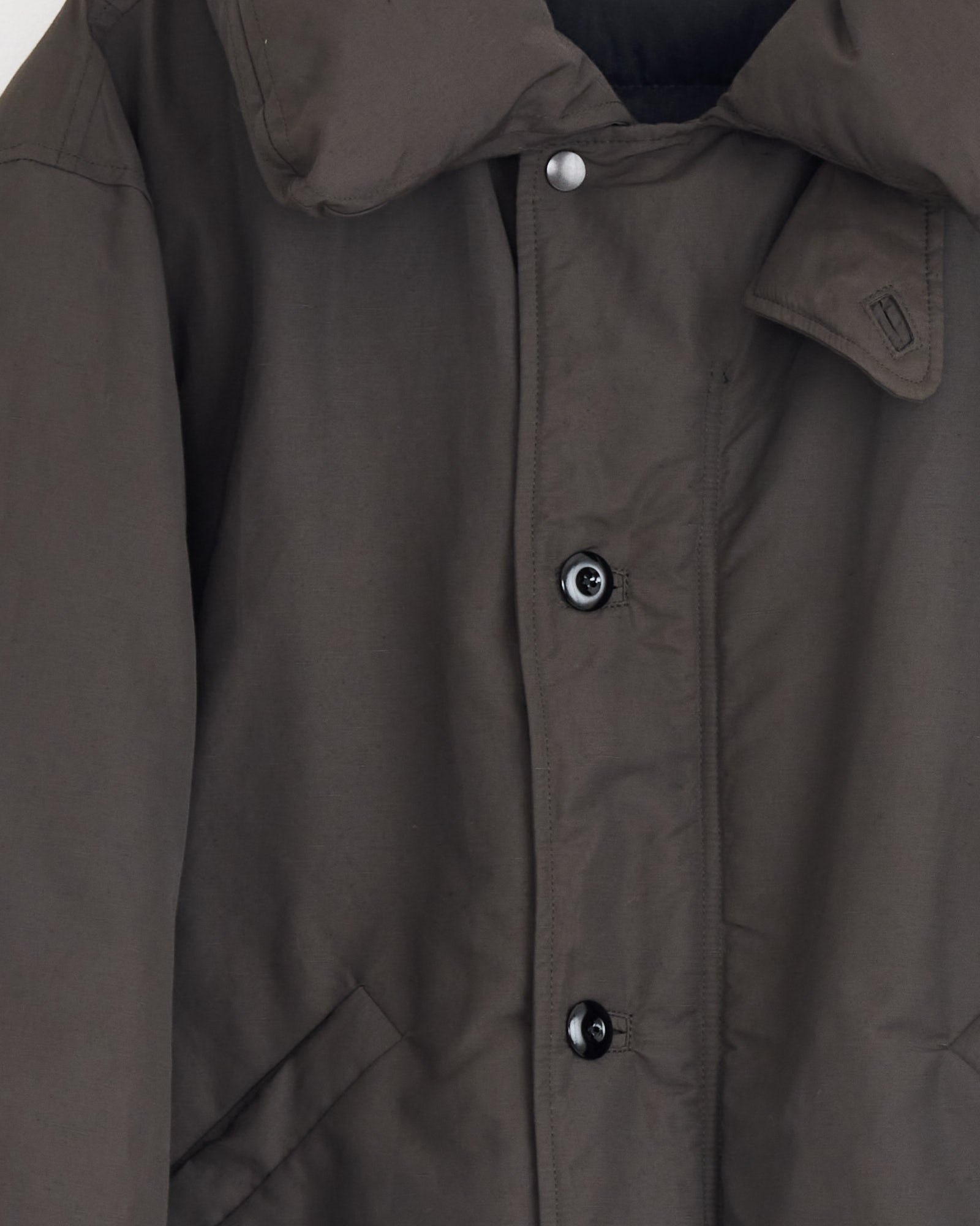 A close-up of the Lemaire Puffer Blouson in Dark Espresso, featuring a high collar, snap buttons, and side pockets. This winter coat is photographed against a plain background.