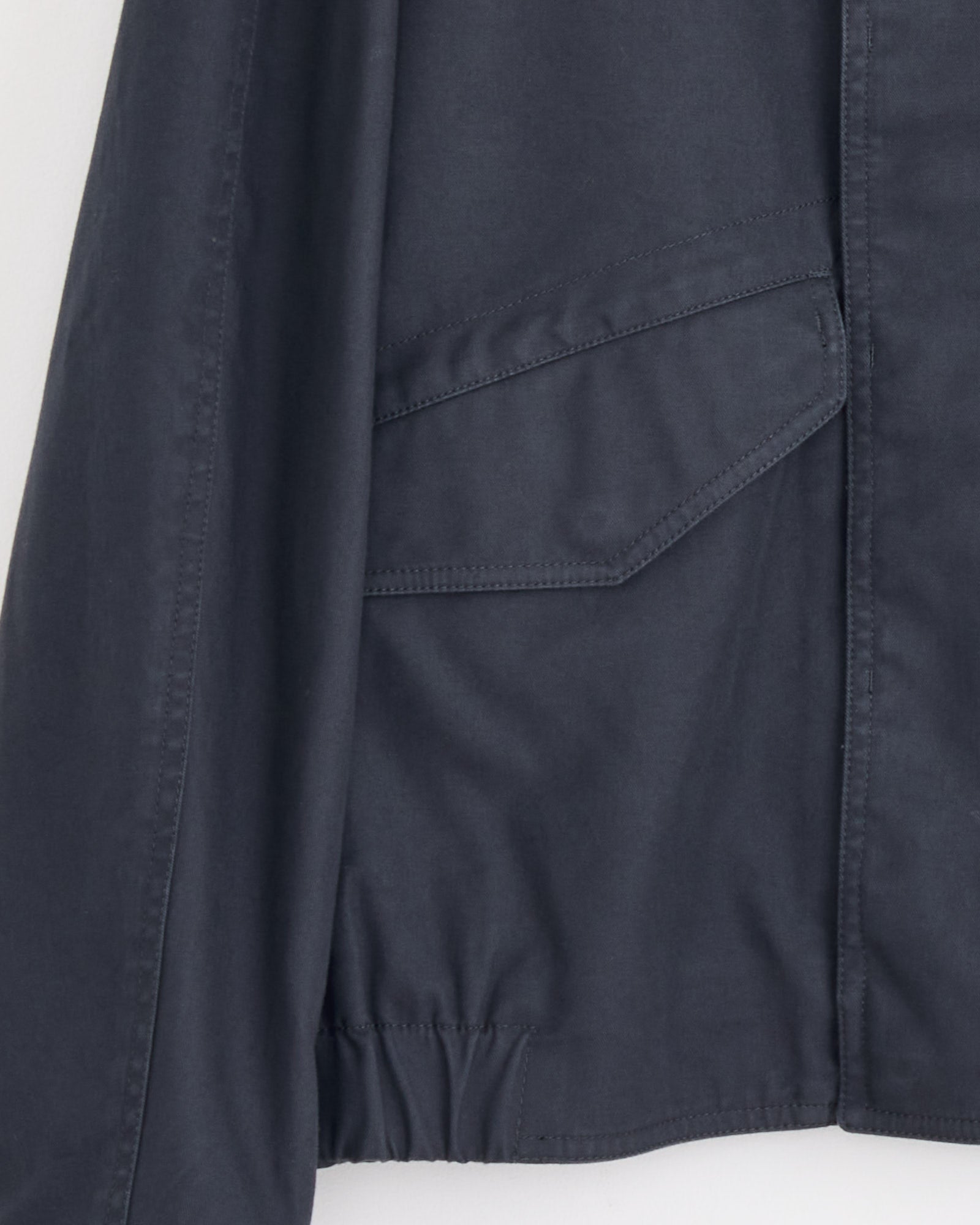 Close-up of the Lemaire Boxy Blouson in Graphite Blue, featuring a flap pocket with visible stitching and a section of the elasticized hem.