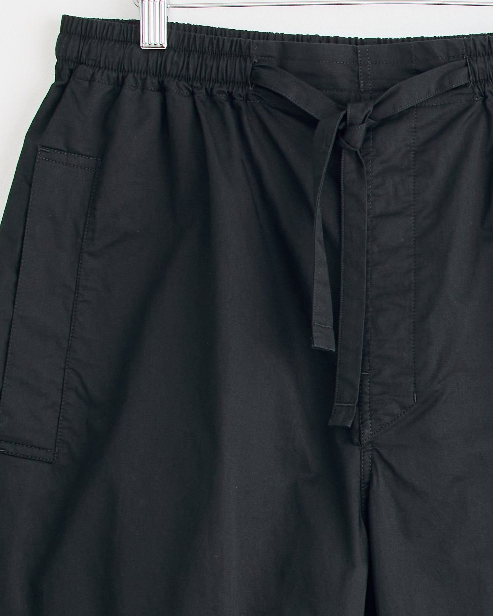 The Pyjama Pant in Black by Lemaire features an elastic waistband and large side pockets, and is shown hanging on a hanger against a white background. For sizing or fit questions, connect with our online chat team.