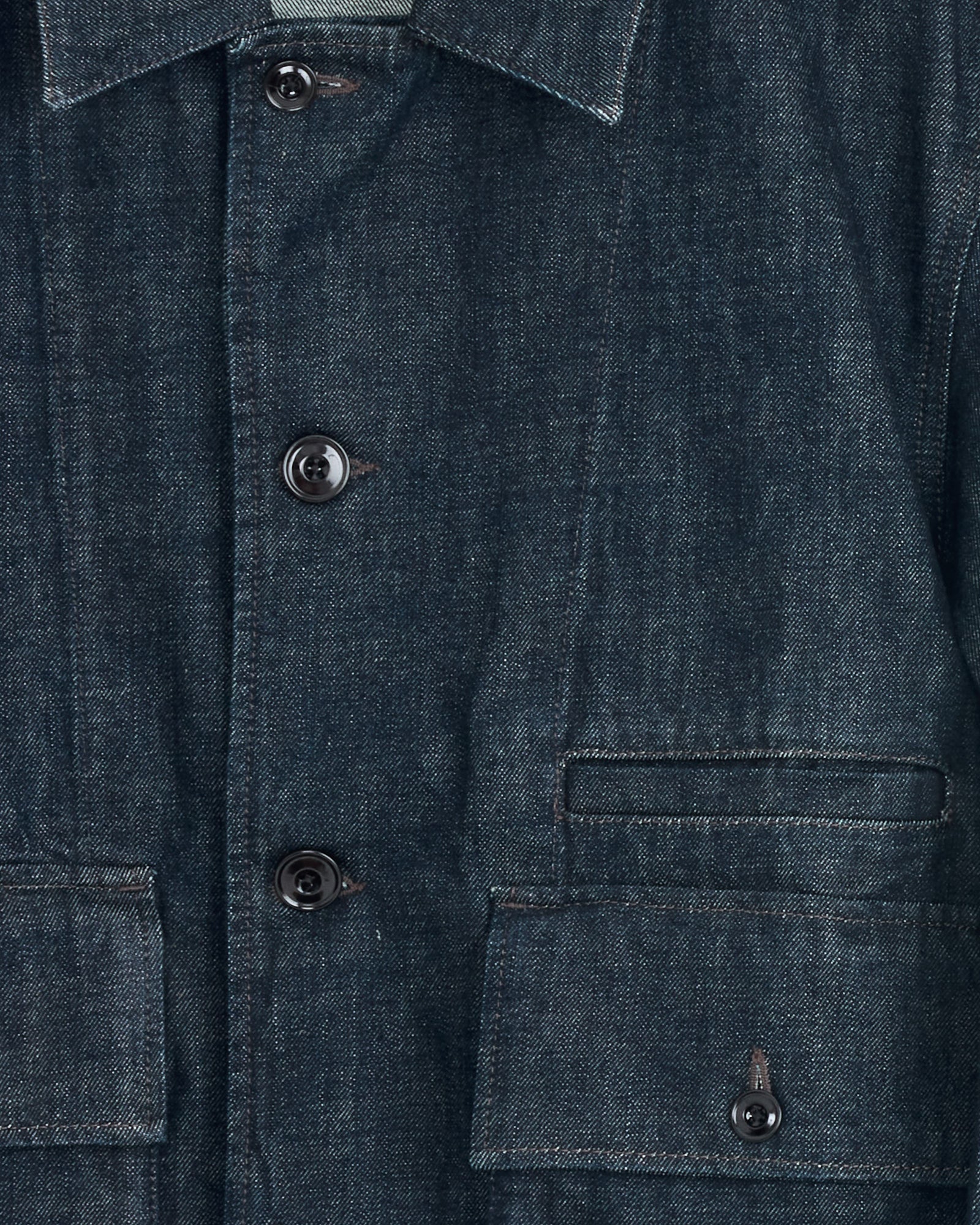 Close-up of the Lemaire Boxy Jacket in Denim Indigo, showcasing black buttons, a collar, two front flap pockets, and visible fabric texture with stitching details.