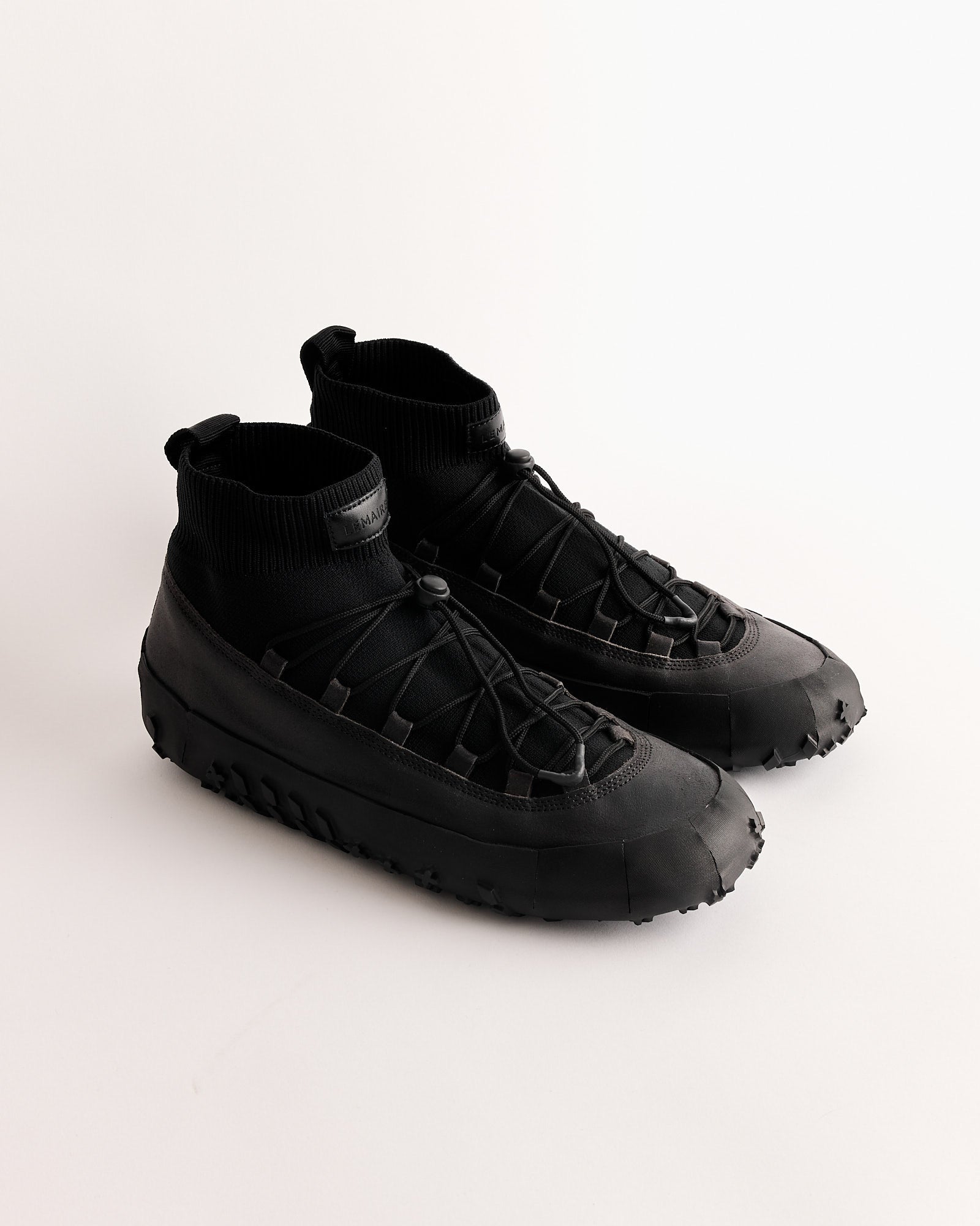 The Lemaire Vibram Wrap On Sneaker in Asphalt features thick, textured waterproof soles, knit ankle collars, and crisscross laces, shown against a plain white background.