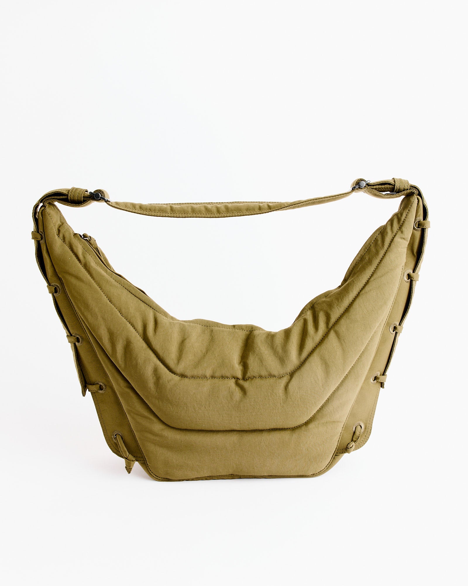The Medium Soft Game Bag in Dusty Khaki by Lemaire is a crescent-shaped, water-repellent nylon bag with a padded, quilted texture and lace-up sides, shown against a plain white background.