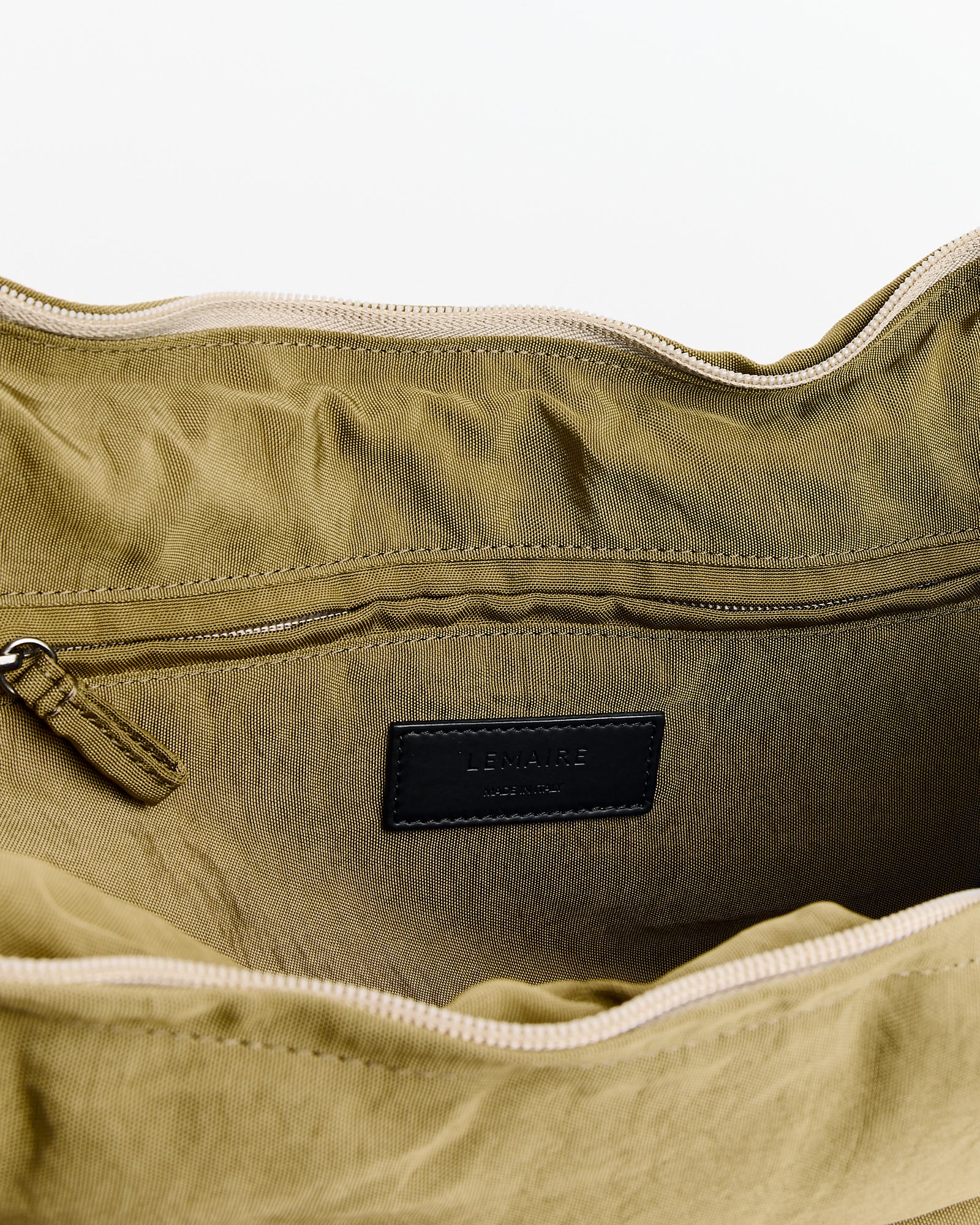 A close-up of the inside of the Lemaire Medium Soft Game Bag in Dusty Khaki, crafted from water-repellent nylon with a fabric lining, inner zip pocket, and a black Lemaire label stitched inside.