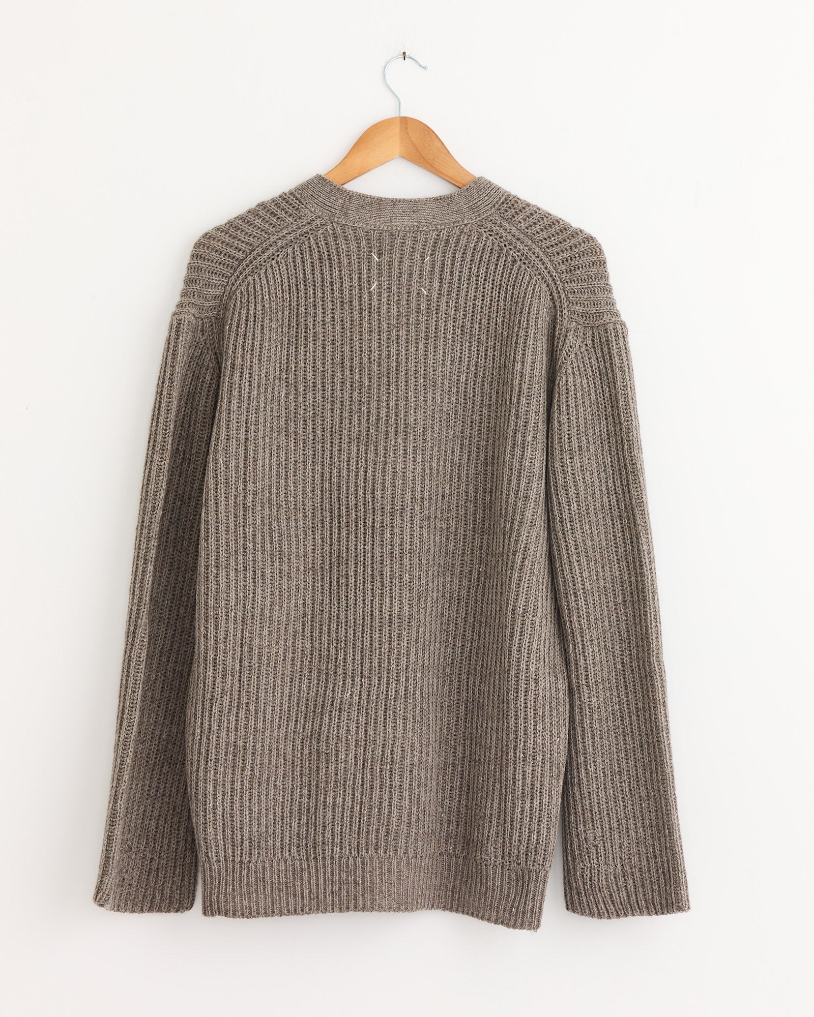 The Maison Margiela Cardigan in Brown, featuring long sleeves and a ribbed texture, is displayed from the back on a wooden hanger against a white wall.