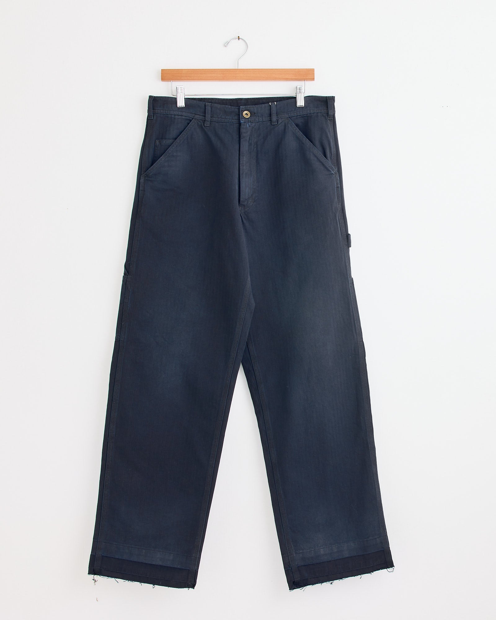Maison Margiela's 5 Pockets Pant in Blue, featuring a high waist, wide legs, side pockets, belt loops, and raw hems, hangs on a wooden hanger against a white background—available at Mohawk General Store.