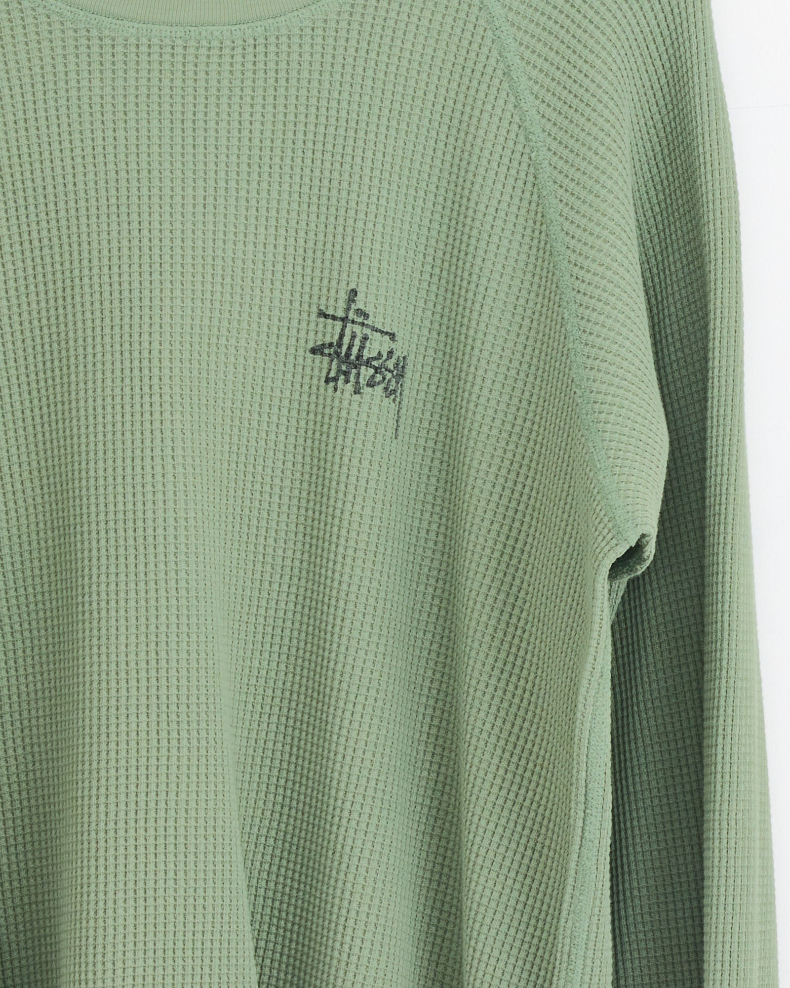 The Stussy Raglan Thermal Basic Stock in Sage is a sage green, waffle-knit cotton long-sleeve shirt with a small black Stussy logo on the upper left chest.
