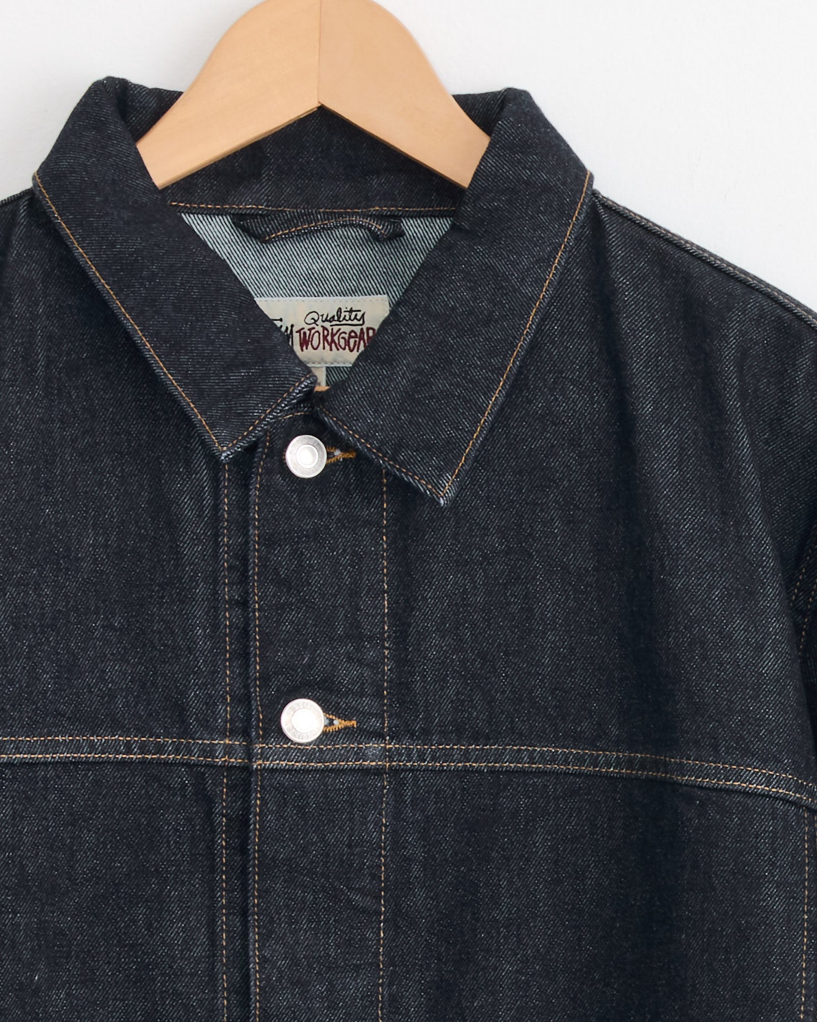 The Stussy Trucker Denim Jacket in Rinsed Indigo, featuring contrast stitching, two white buttons, a pointed collar, and a relaxed boxy fit, hangs on a wooden hanger against a plain white background.