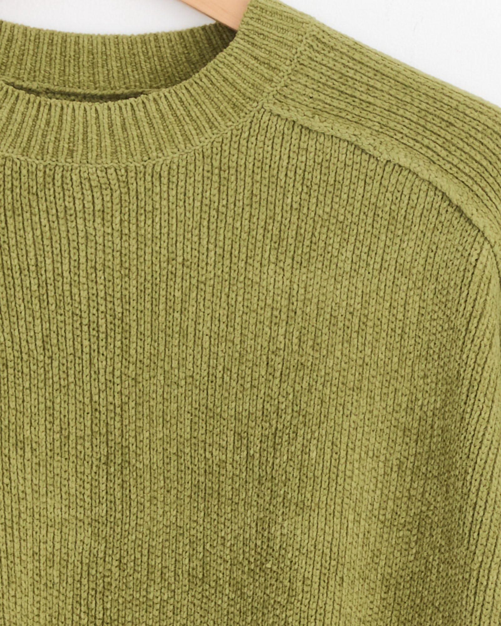 Close-up of the Stussy Exposed Seam Sweater in Green, featuring ribbed knit textured fabric, a round neckline, and subtle exposed seams as it hangs on a wooden hanger.