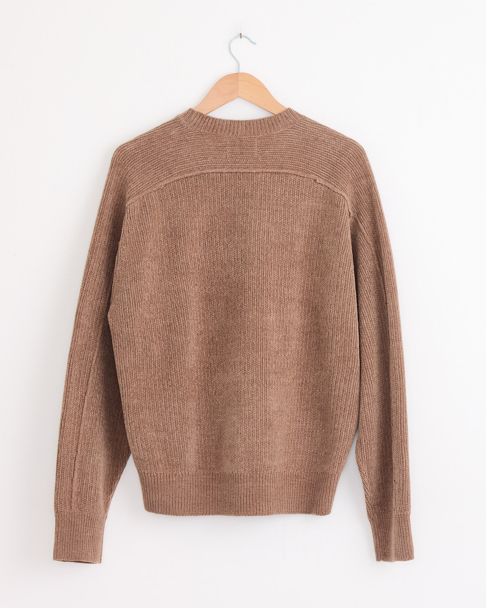 The Stussy Exposed Seam Sweater in Brown, featuring long sleeves and ribbed knit, is shown from the back on a wooden hanger against a plain white wall.