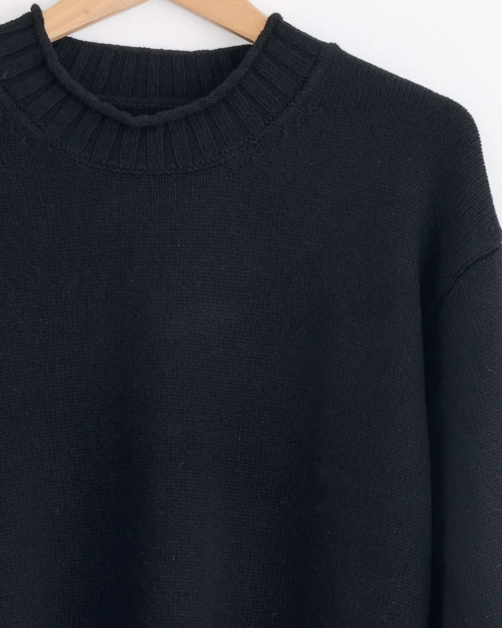 A close-up of the Stussy Tonal Mock Neck Sweater in Black, featuring a ribbed neckline, hanging on a wooden hanger against a white background.