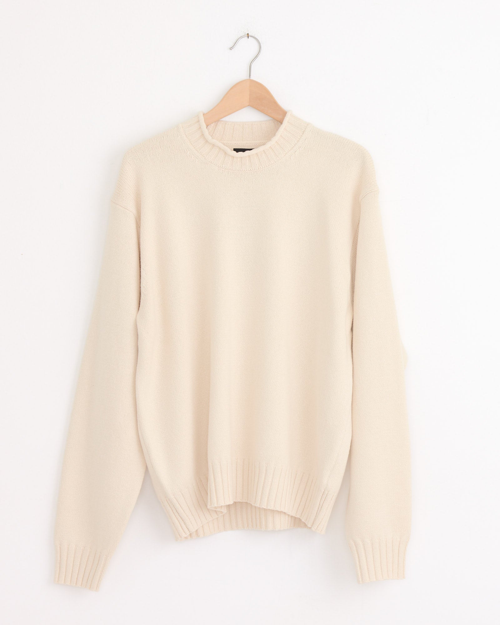 The Stussy Tonal Mock Neck Sweater in Natural, featuring long sleeves and a cream hue, is shown on a wooden hanger against a white background.
