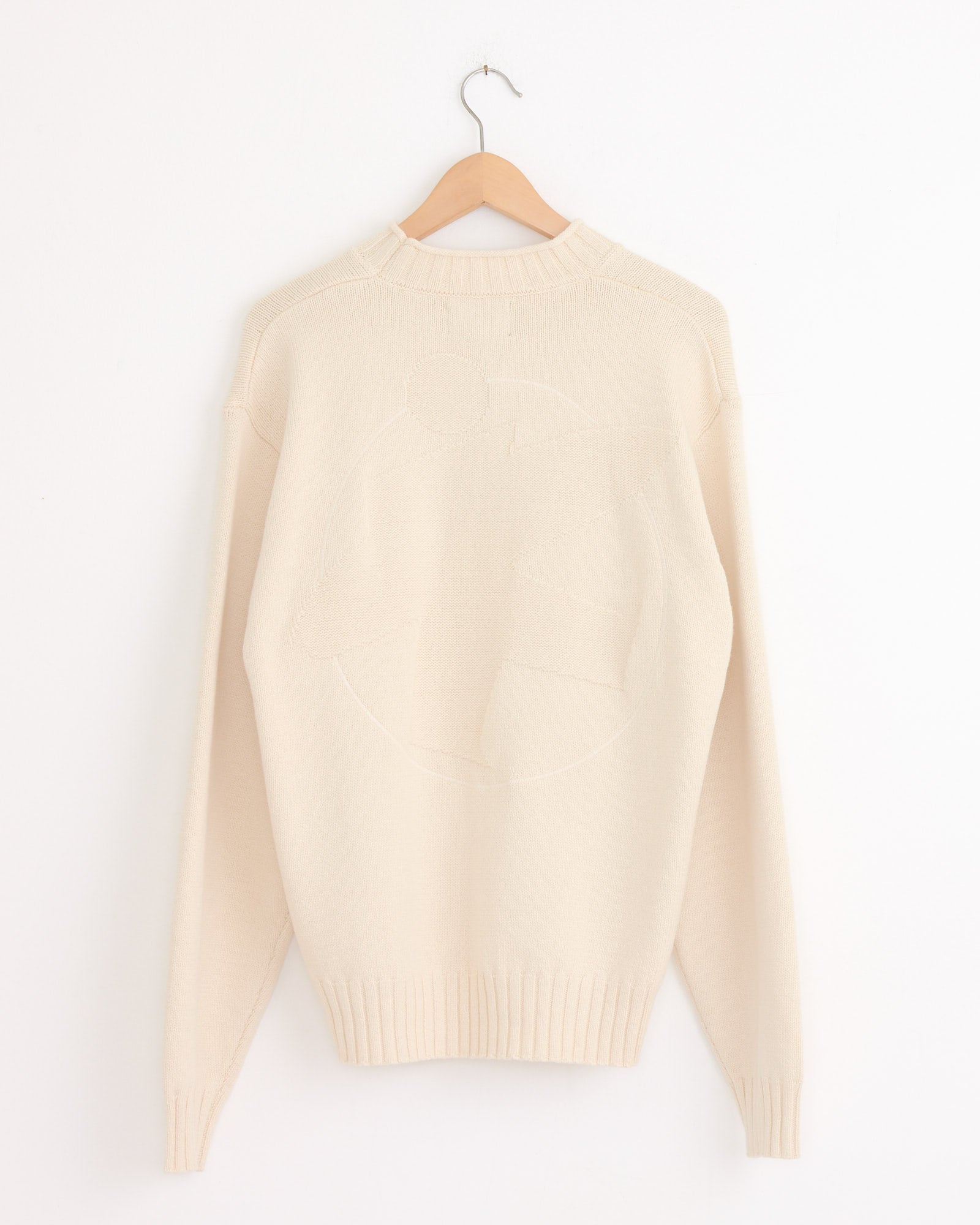 The Stussy Tonal Mock Neck Sweater in Natural hangs on a wooden hanger against a white wall, featuring ribbed neckline, cuffs, and hem, and a subtle textured back detail.
