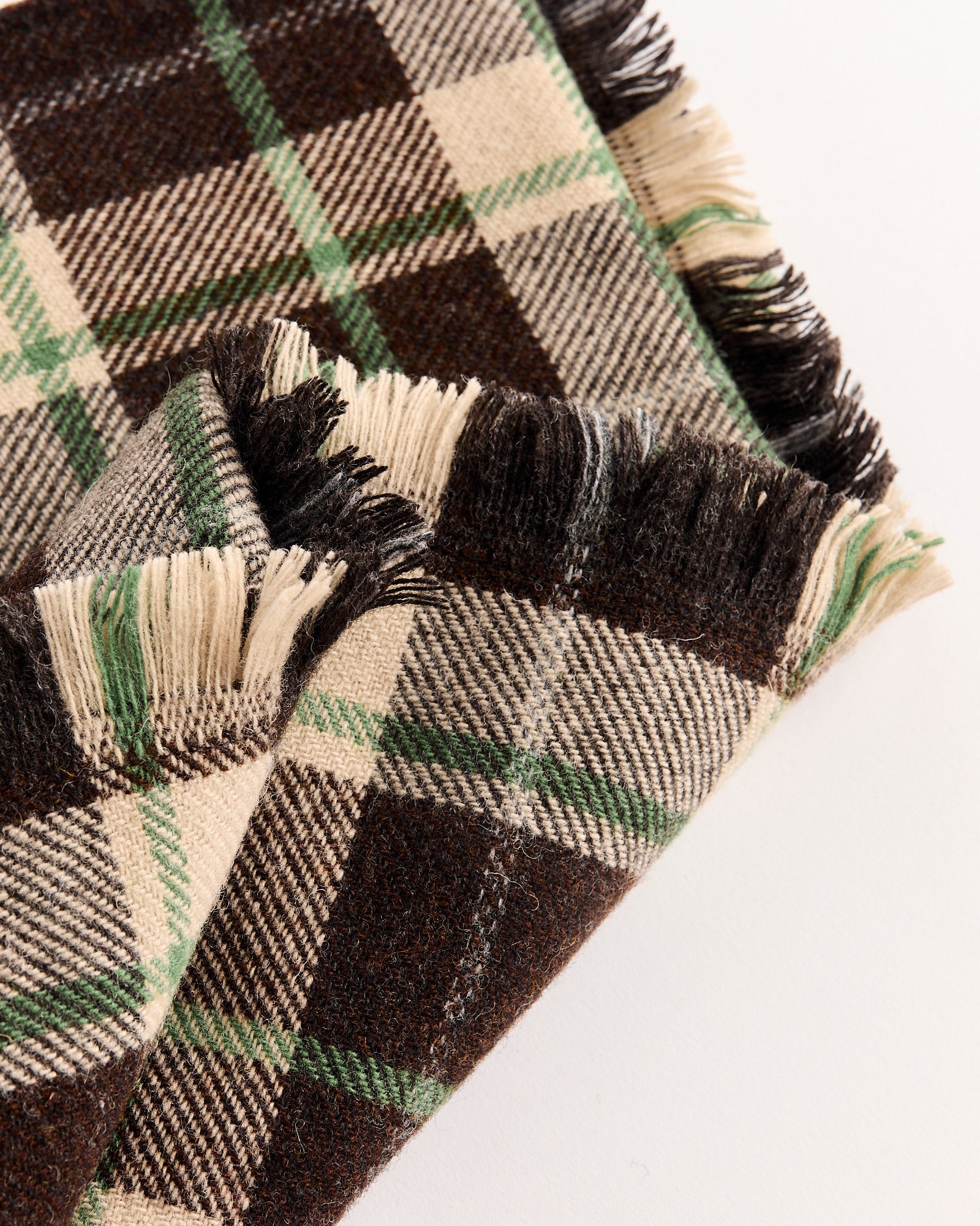 A close-up of the Bode Woodcrest Scarf in Brown/Green by Bode, featuring a brown, green, and cream plaid pattern with frayed edges that highlight the rich texture and classic weave of this stylish scarf.