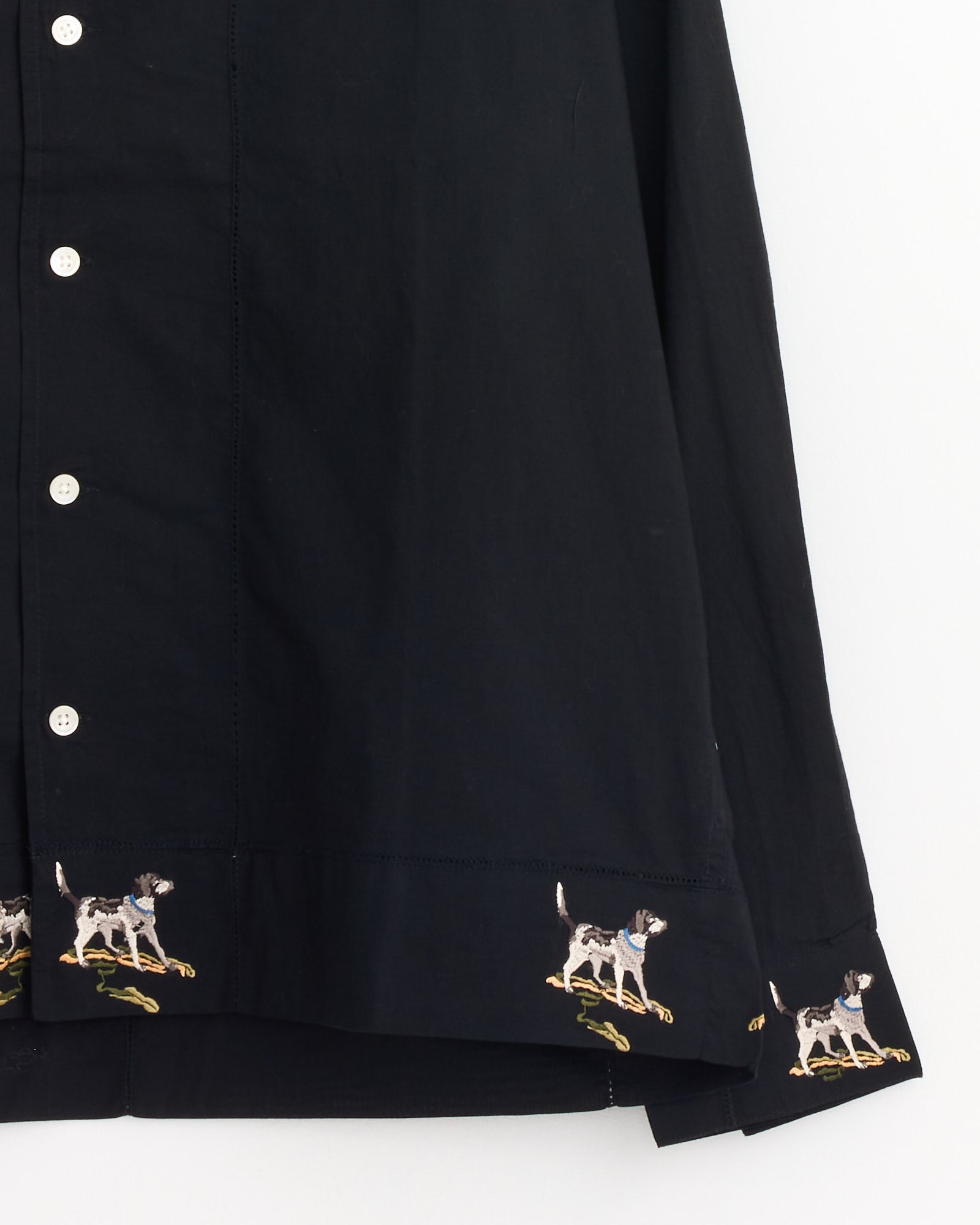 The Bode Pointer Shirt in Black is a cotton button-up with white buttons, featuring an embroidered dog motif near the hem, with dogs walking on green patches in Bode’s signature playful style.