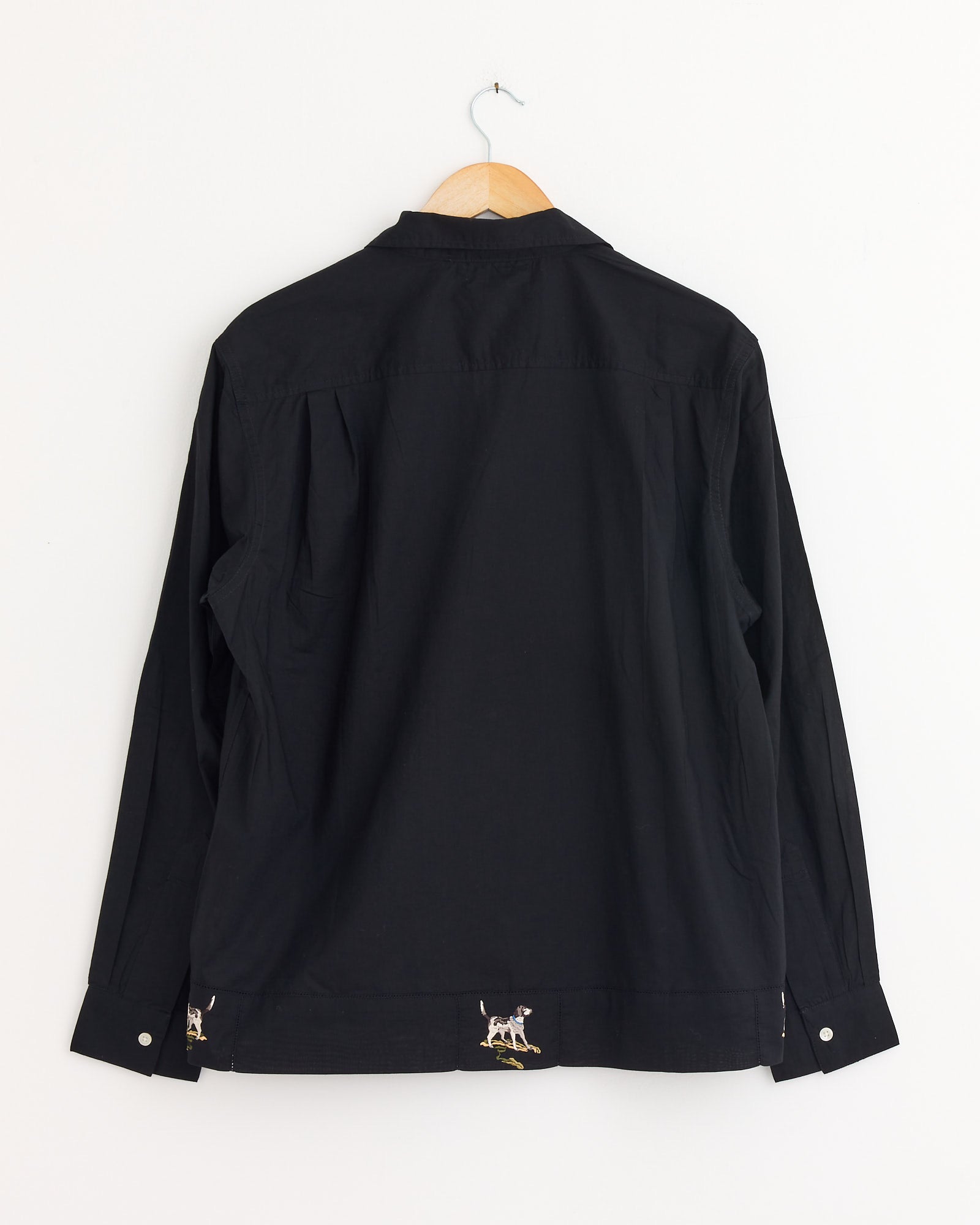 The Bode Pointer Shirt in Black, made of cotton, is displayed from the back on a wooden hanger against a white wall, featuring small dog embroidery near the bottom hem—highlighting Bode’s signature style.