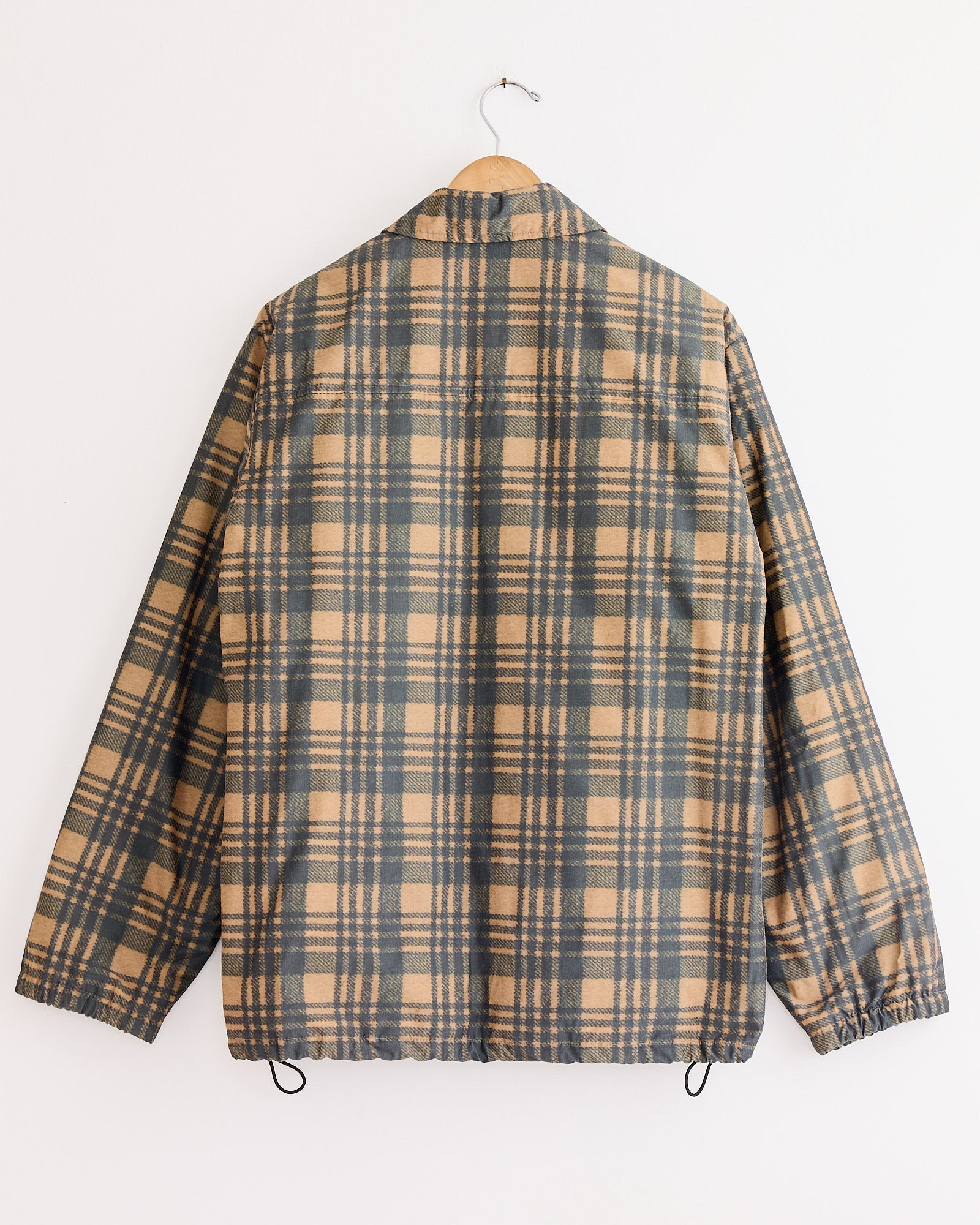 The Dries Van Noten Vorries 2026 Jacket in Tan, a long-sleeved men's jacket with a tan and dark gray plaid pattern, is shown from the back on a wooden hanger. This lined jacket features a comfortable polyester-cotton blend.