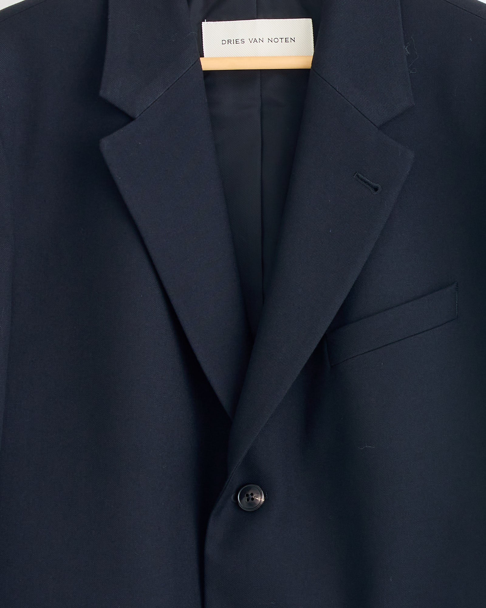 A close-up of the Dries Van Noten Kiel 2246 Suit in Black showcases its loose fit, single button, and notched lapel, displayed on a hanger with the brand's label inside the collar.